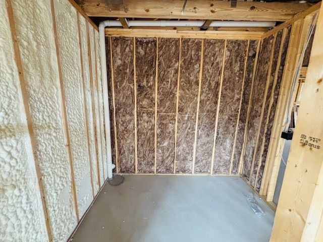 Room under construction: studs, insulation, spray foam, concrete floor, pipes.