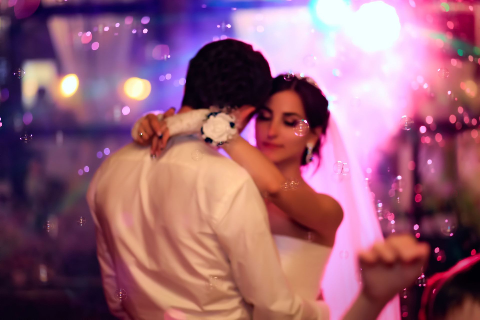 Couple slow dancing at a colorful party, with pink and purple lights in the background