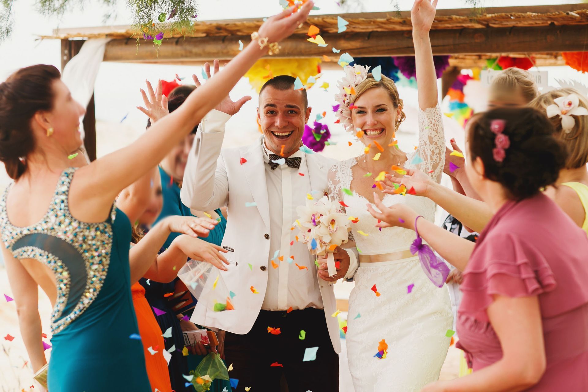 Confetti-filled wedding celebration with a smiling couple and guests dancing outdoors