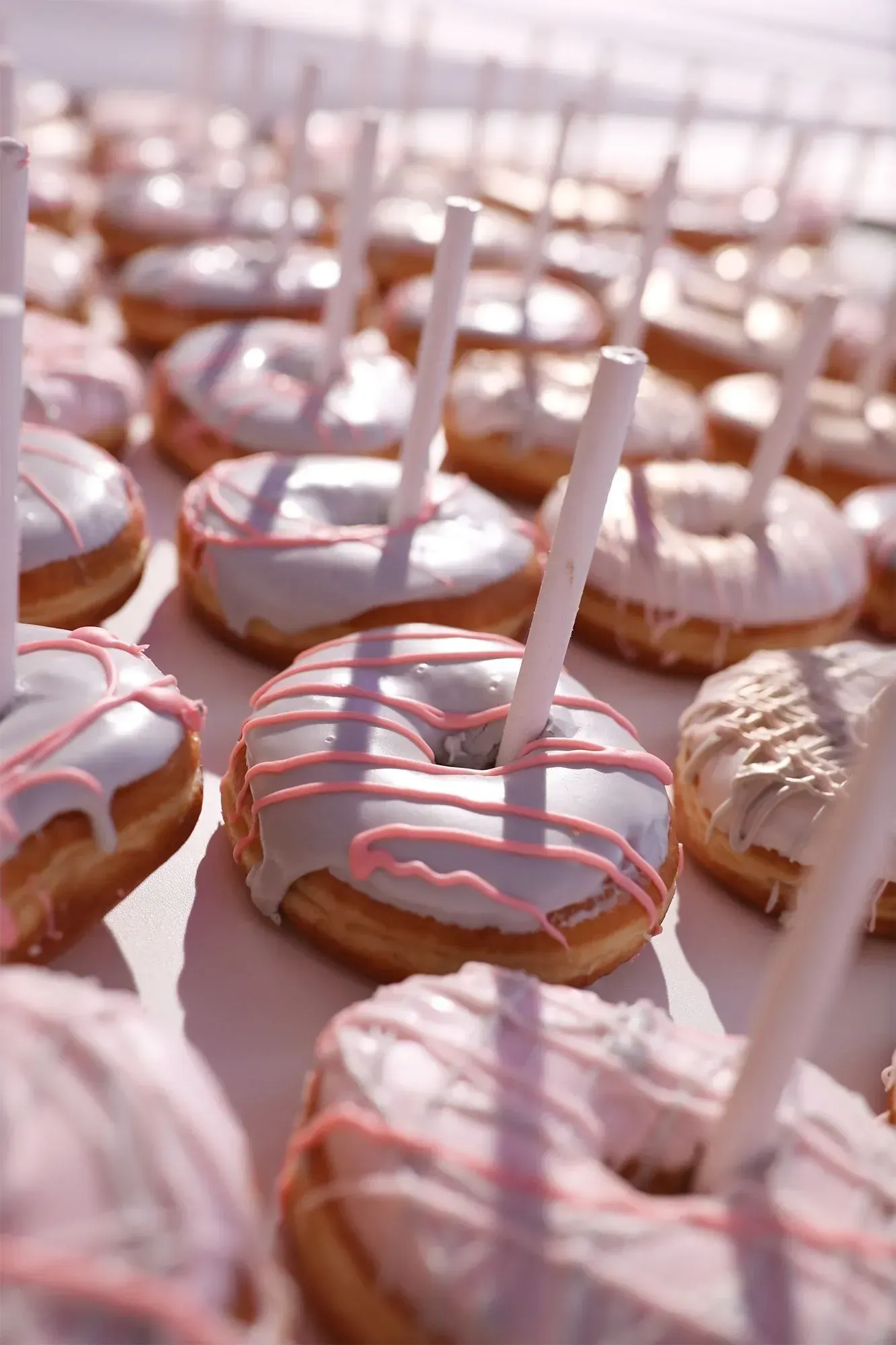 Pink-iced donuts with white sticks arranged on trays, lit by soft sunlight