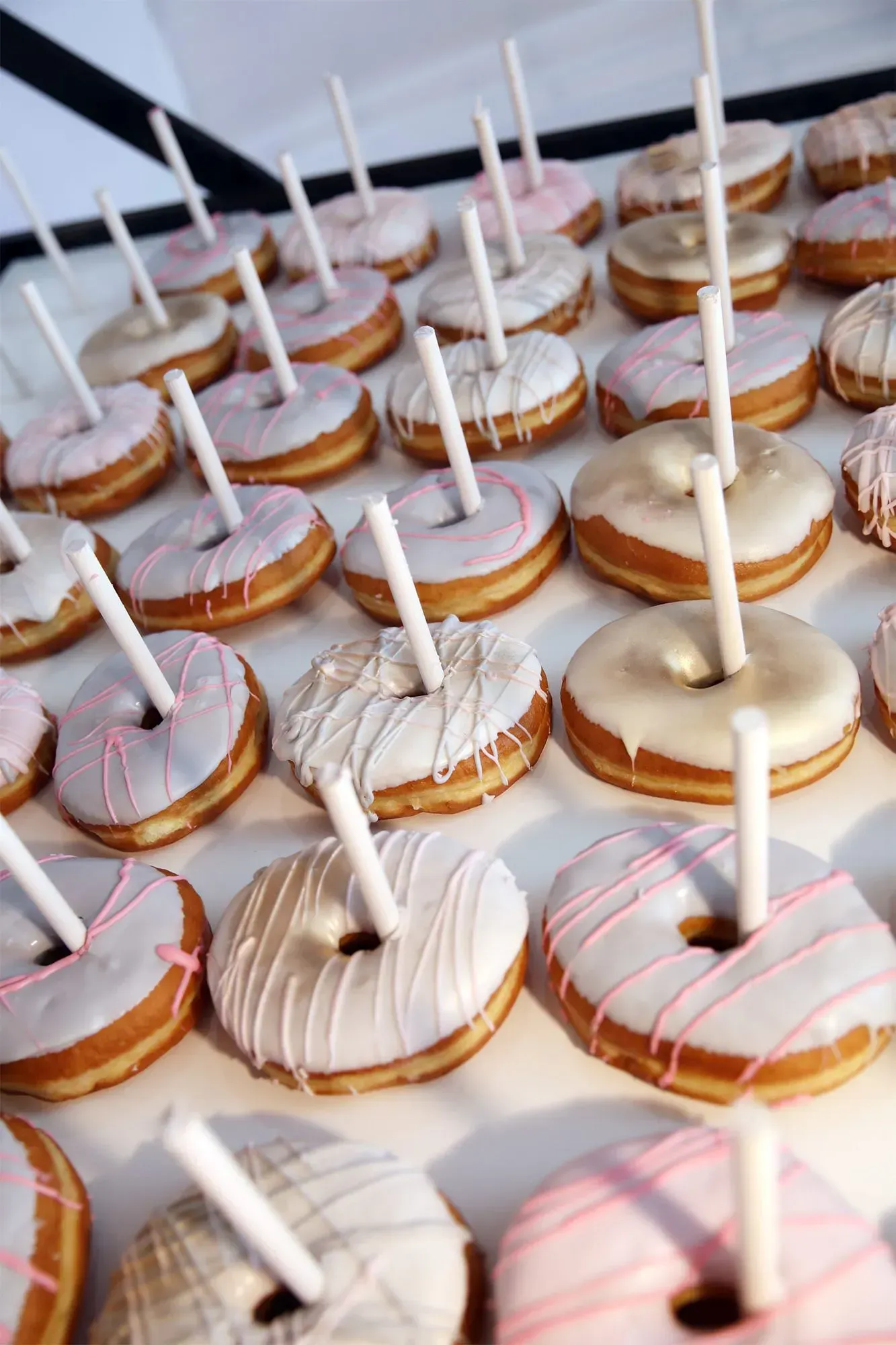 Tray of assorted iced donuts with white stick toppers, arranged in rows on a table.