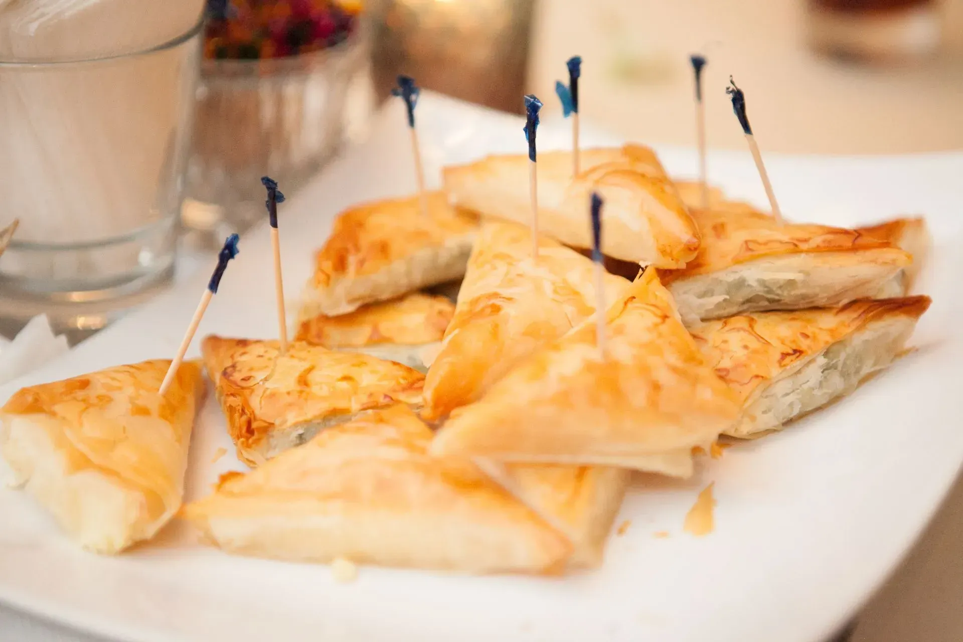 Toasted pastry triangles on a white platter, topped with blue picks, at a table setting