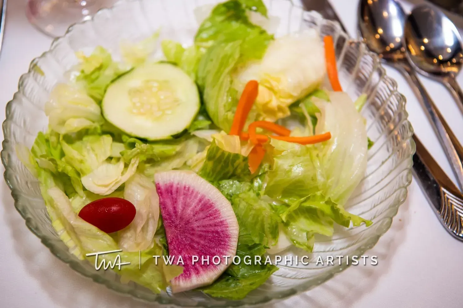 Glass bowl of fresh salad with lettuce, cucumber, radish, and carrot strips on a table