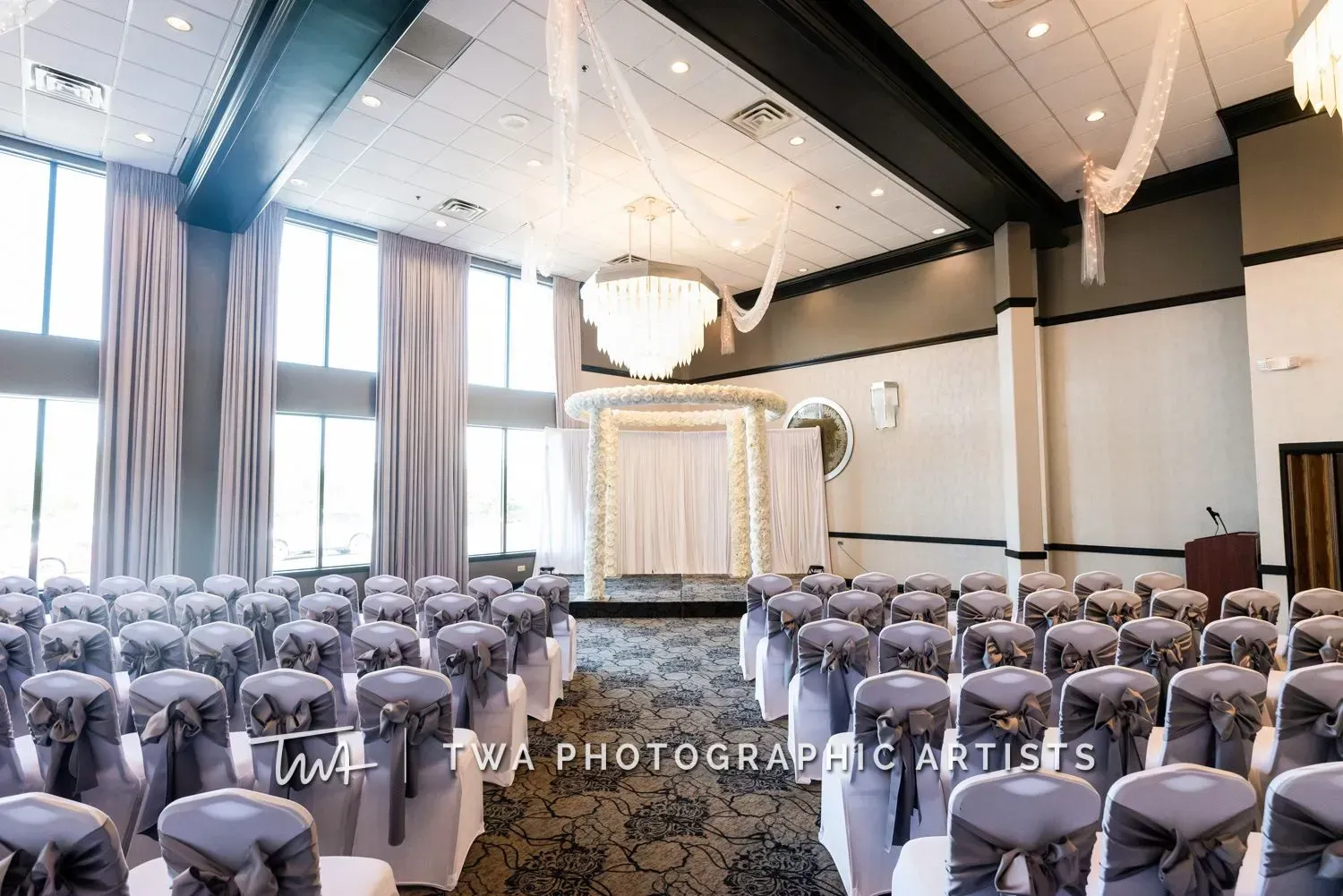 Elegant wedding ceremony setup with rows of white chairs and a decorated altar in a bright hall