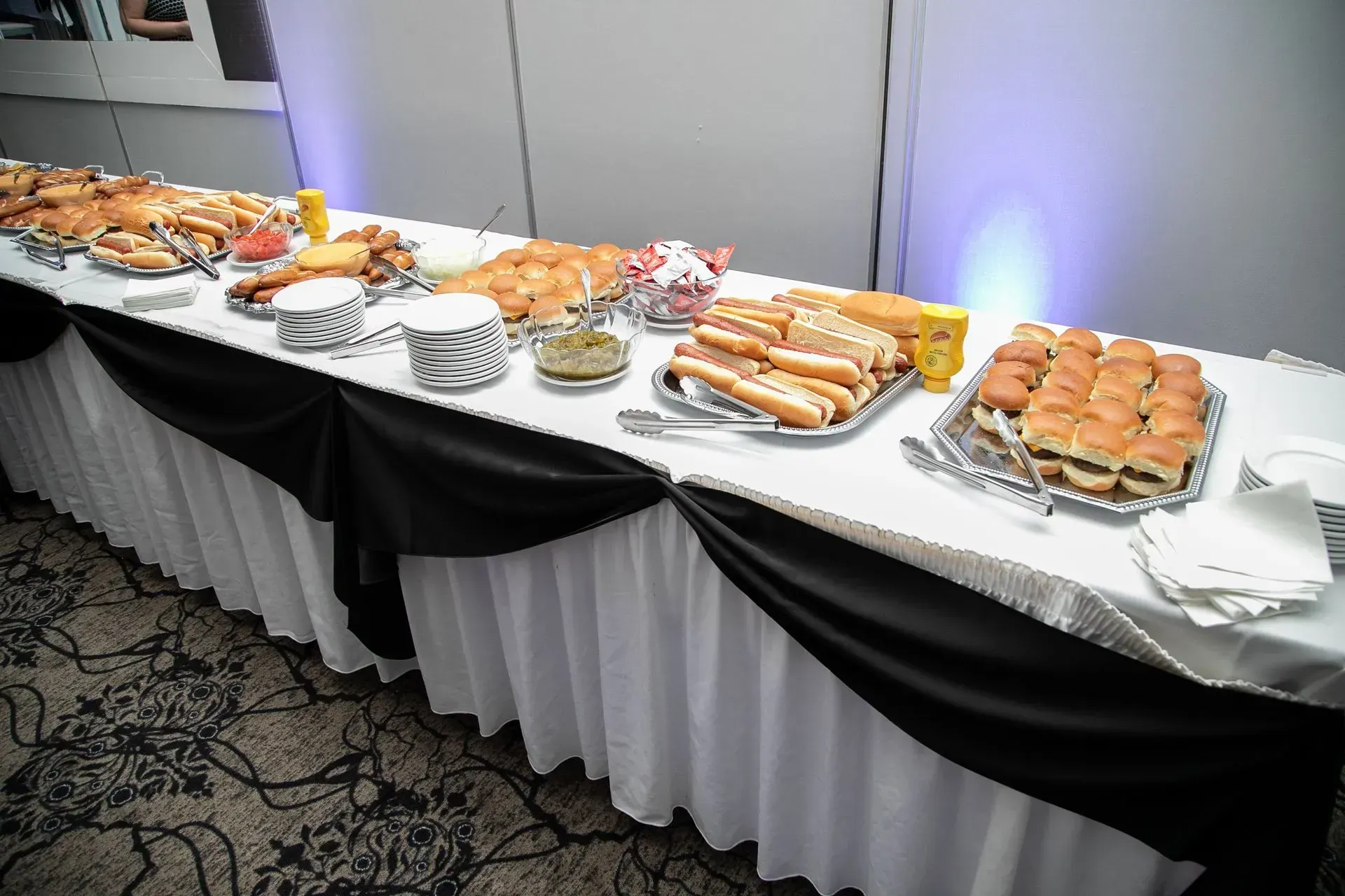 Buffet table with pastries, sandwiches, and desserts on white-and-black linens in a banquet room