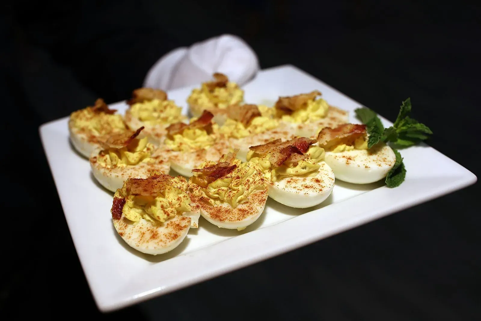 Deviled eggs topped with paprika on a white platter, garnished with parsley.