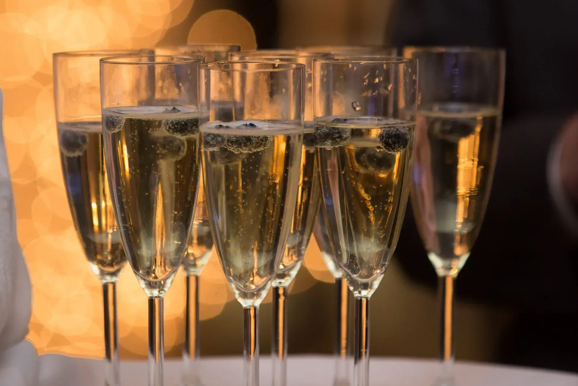 Glasses of champagne lined up on a table with warm, golden lighting
