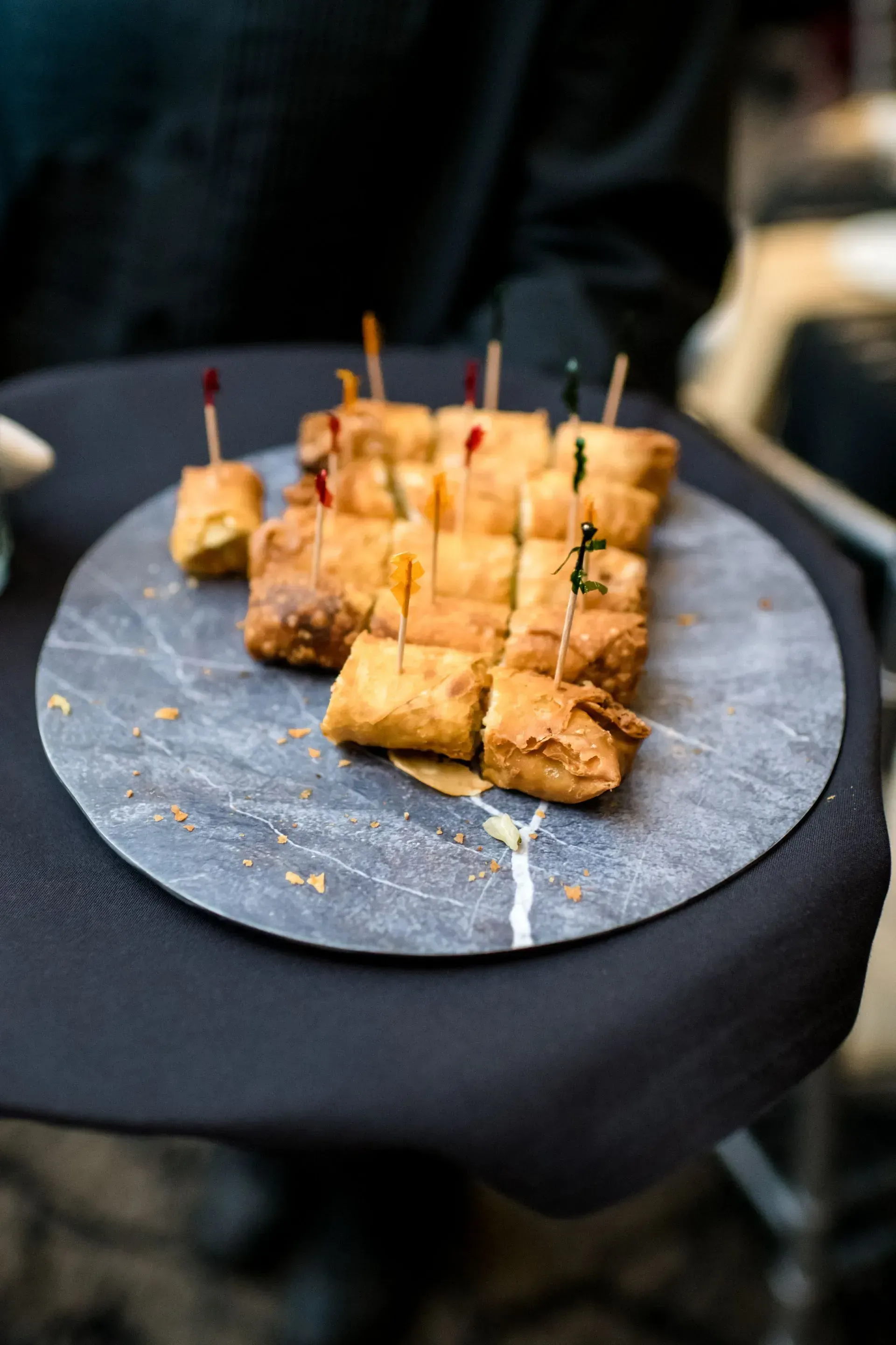 Skewered bite-size appetizers on a black serving tray at an event table