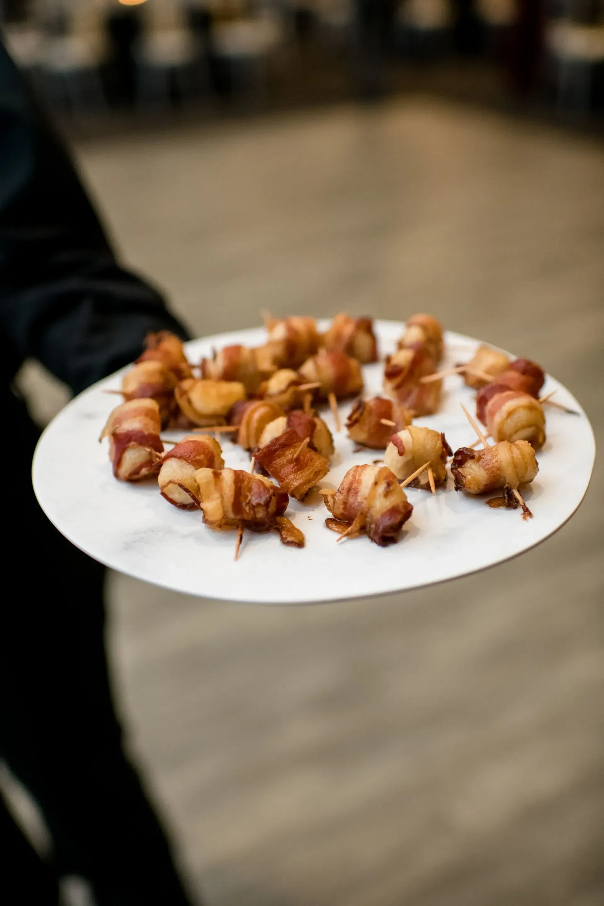 Plate of bacon-wrapped appetizers held by a person indoors