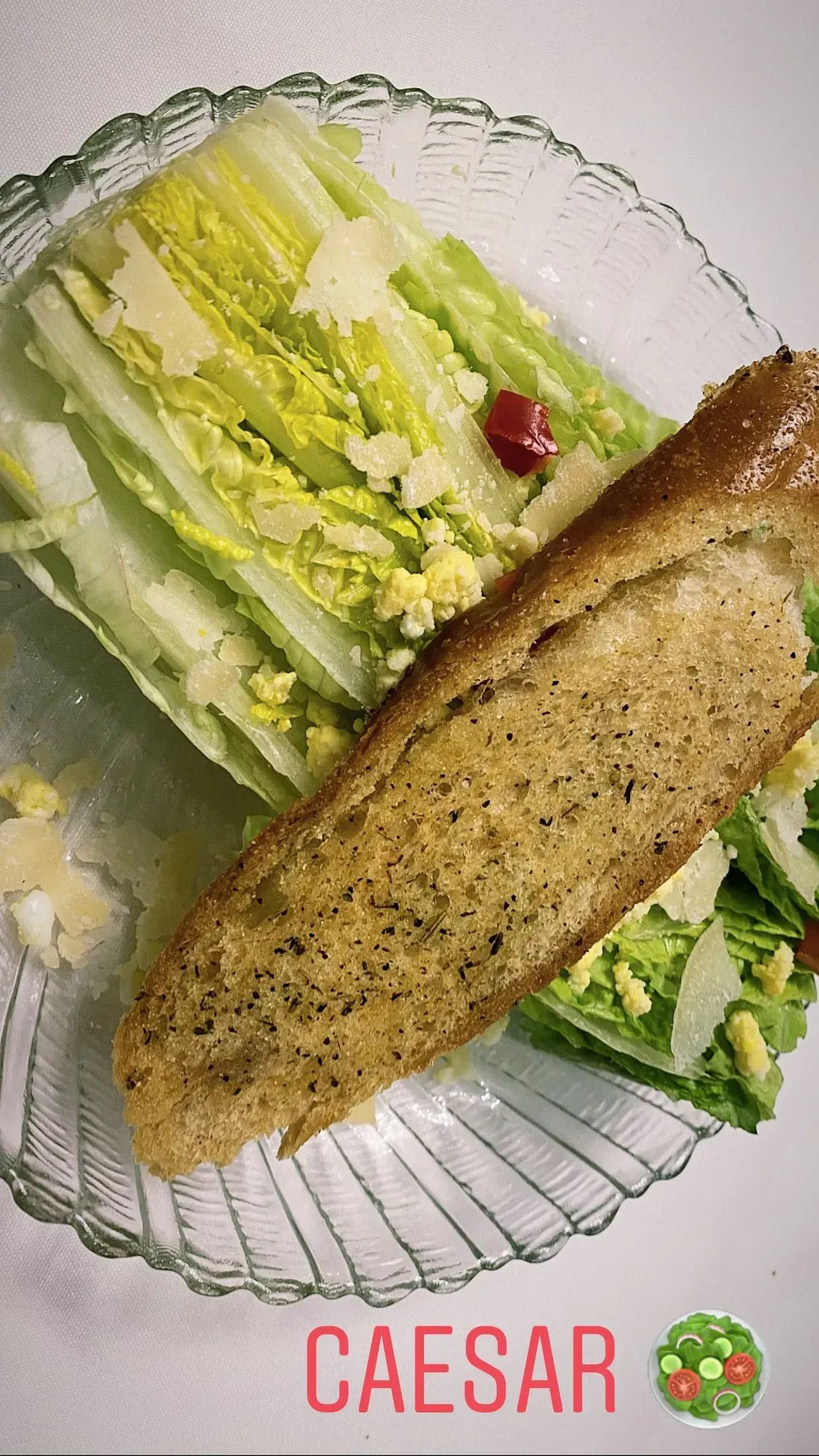 Caesar salad with romaine, croutons, grated cheese, and a breadstick on a glass plate.