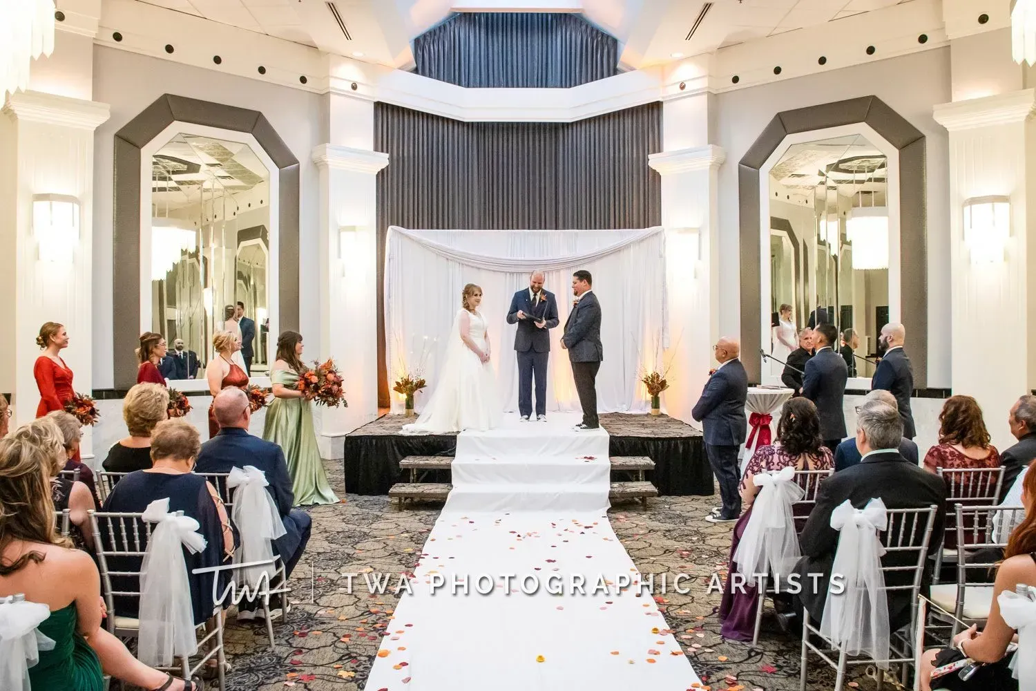 Wedding ceremony in a bright white chapel, with bride and groom at the altar and guests seated on both sides