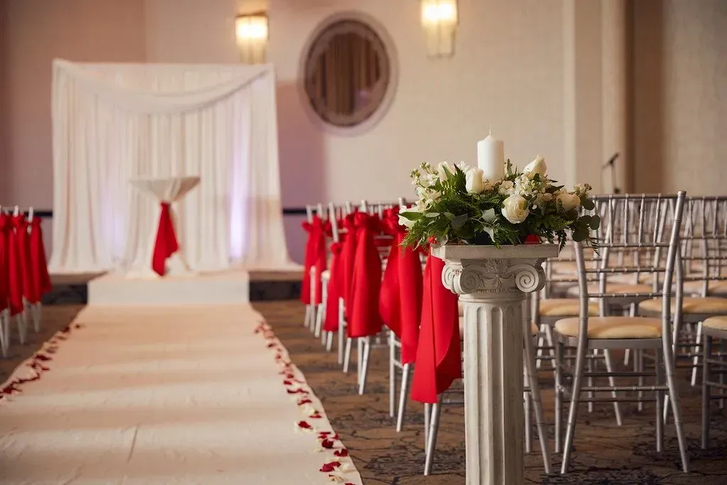 Decorated wedding aisle with red chair sashes and a floral arrangement at the front