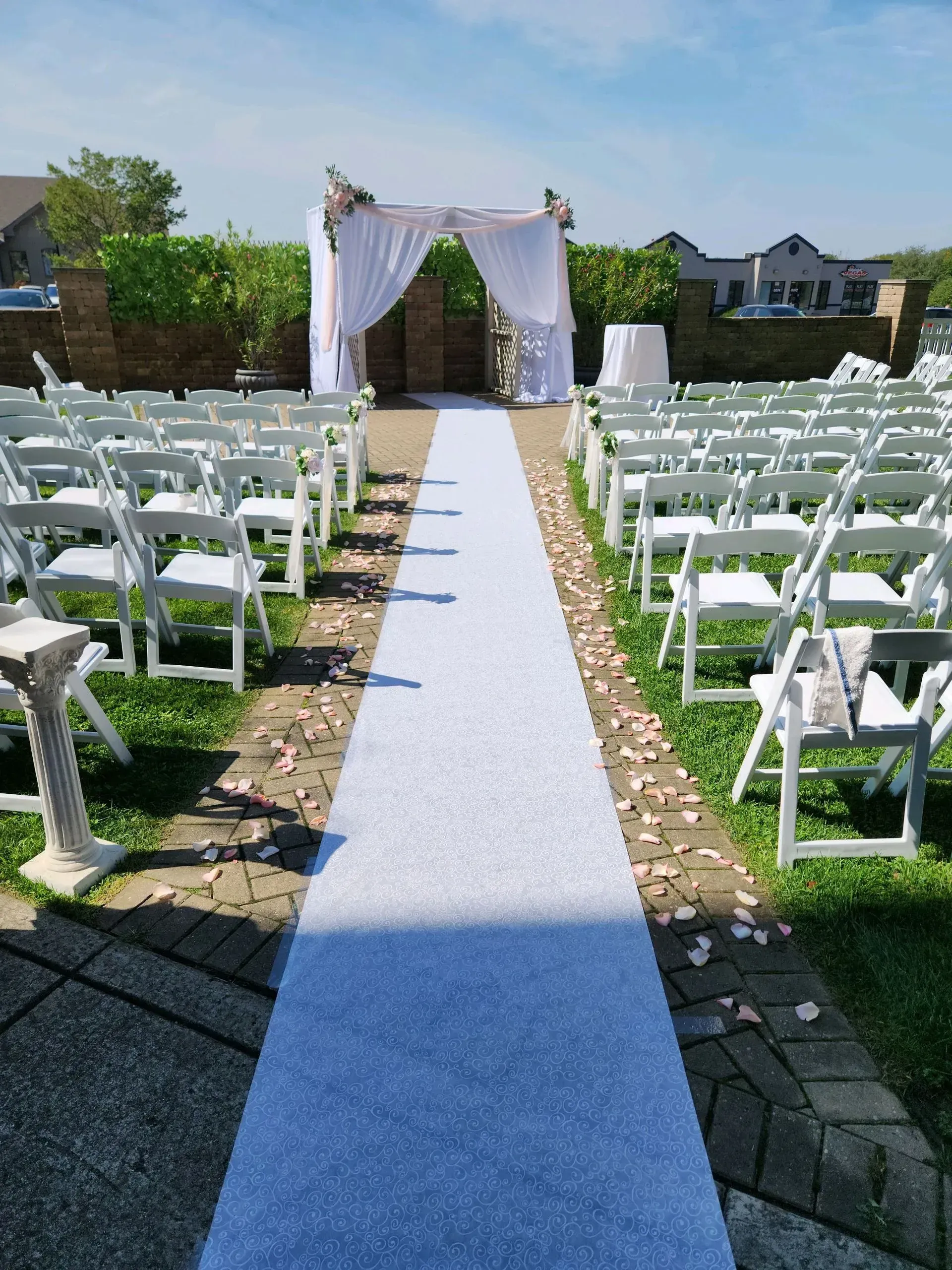 Outdoor wedding aisle with white chairs, blue carpet, and a decorated arch under a bright sky