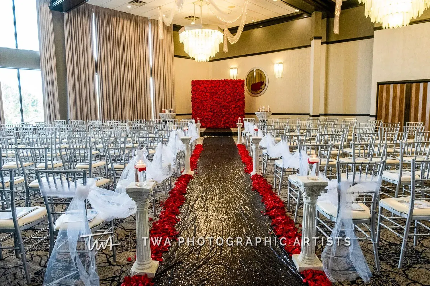 Elegant wedding reception setup with white chairs, long tables, and red aisle runner leading to a red backdrop