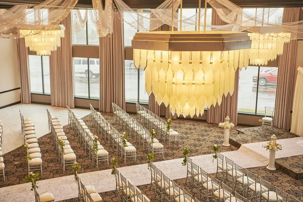 Elegant indoor wedding reception with rows of floral chairs, long tables, and gold chandeliers in a bright hall