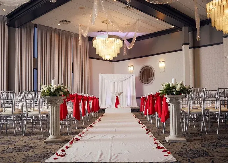 Decorated wedding aisle with white runner, red chair bows, and floral arrangements in a banquet hall