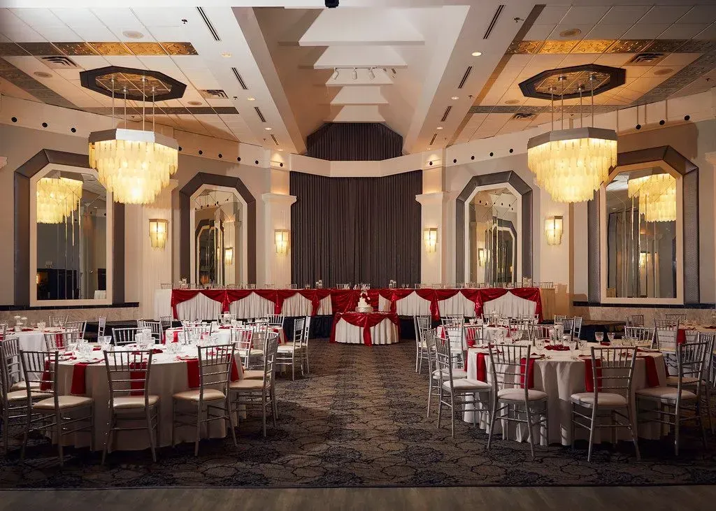 Elegant banquet hall with round dining tables, red chairs, chandeliers, and mirrored walls