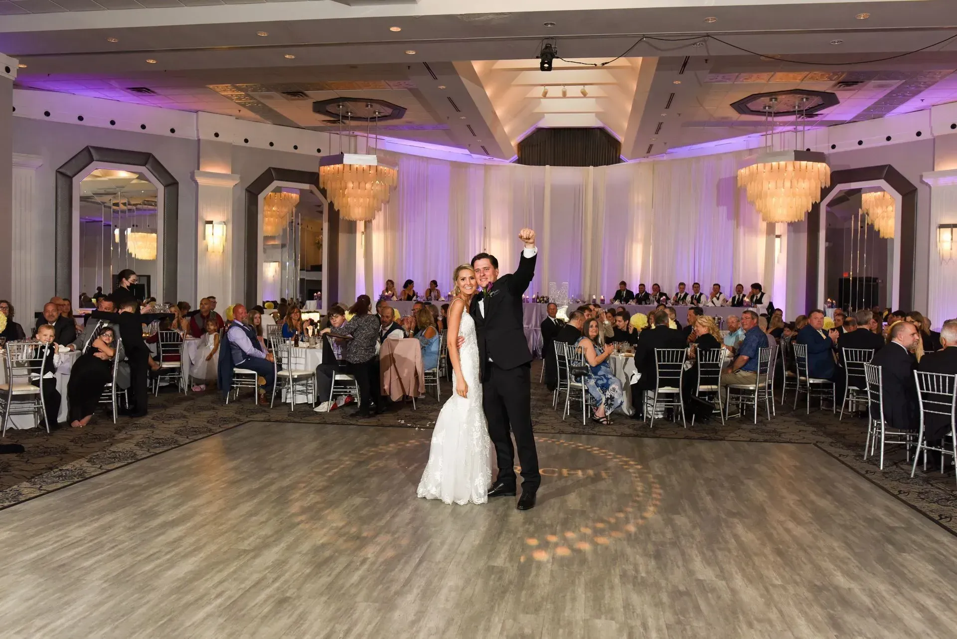 Bride and groom dancing in a decorated wedding reception hall with guests seated at tables