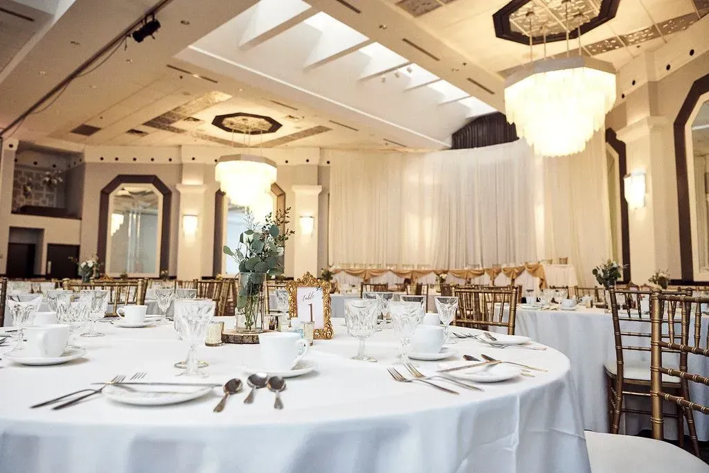 Elegant banquet hall with round tables, white tablecloths, chandeliers, and gold chairs arranged for an event