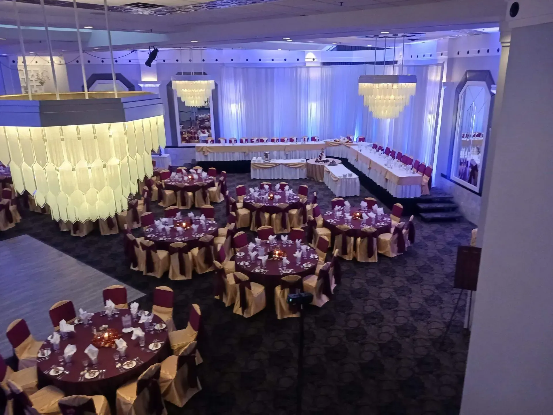 Elegant banquet hall with round tables, gold chairs, and blue-purple uplighting ready for an event