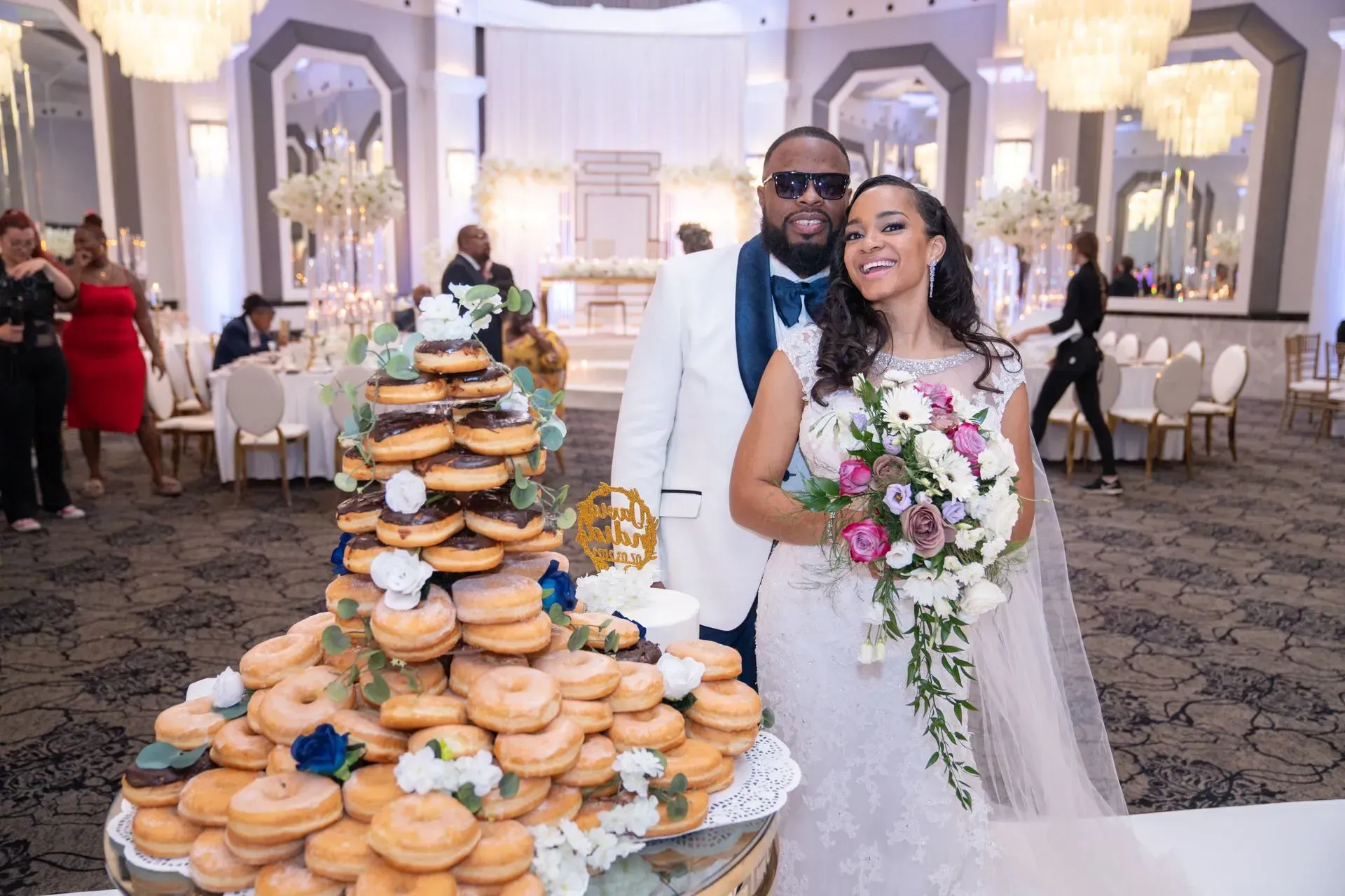Wedding couple posing beside a large tower of pastries in a decorated reception hall