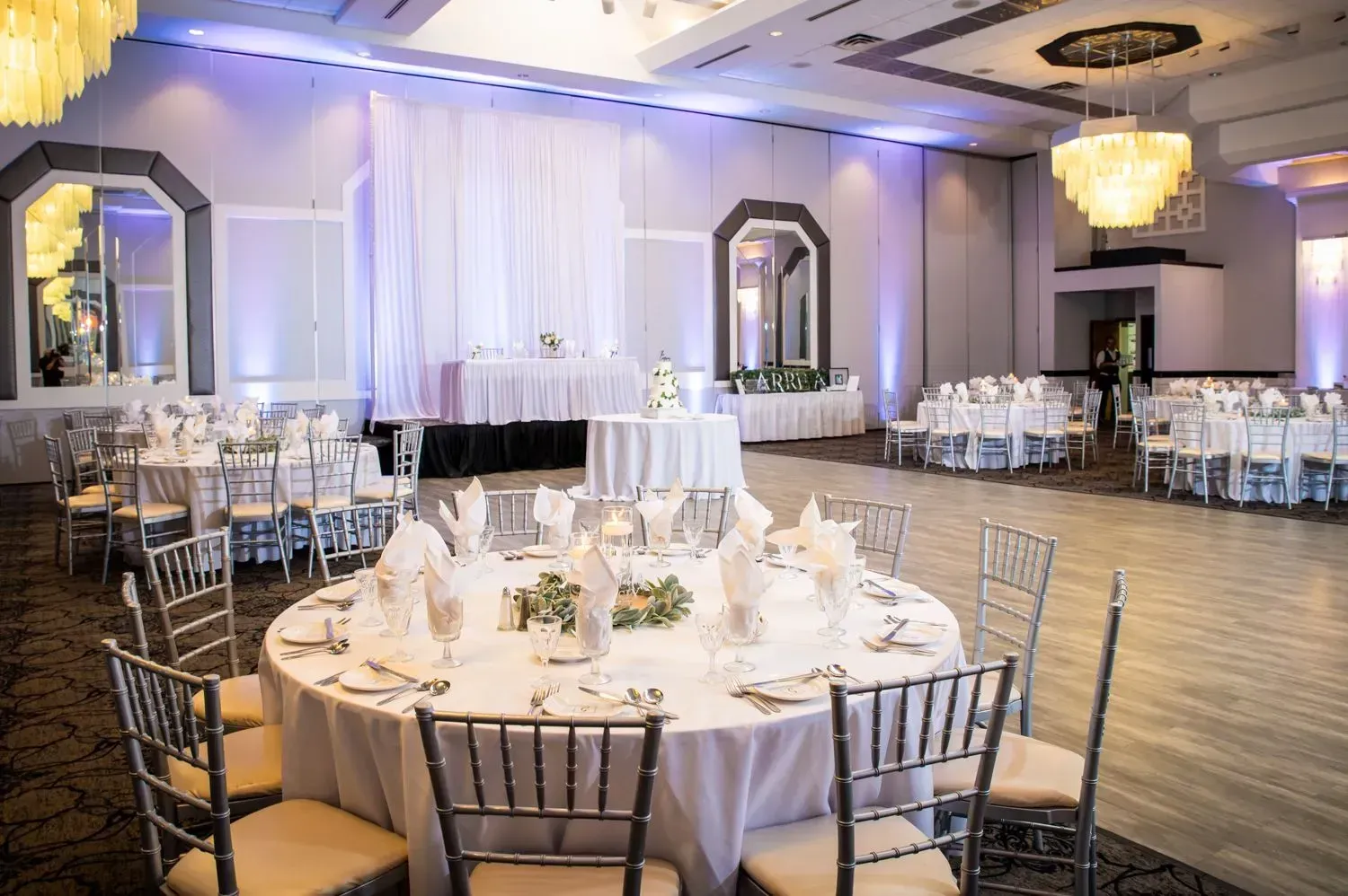 Elegant banquet hall with round dining tables, white tablecloths, and a lit dance floor stage