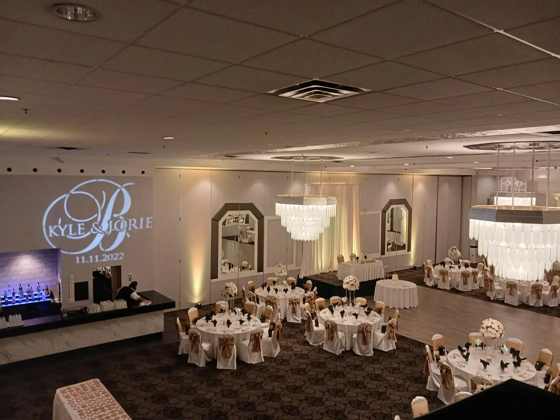 Elegant banquet hall with round tables, white chair covers, chandeliers, and a lit stage