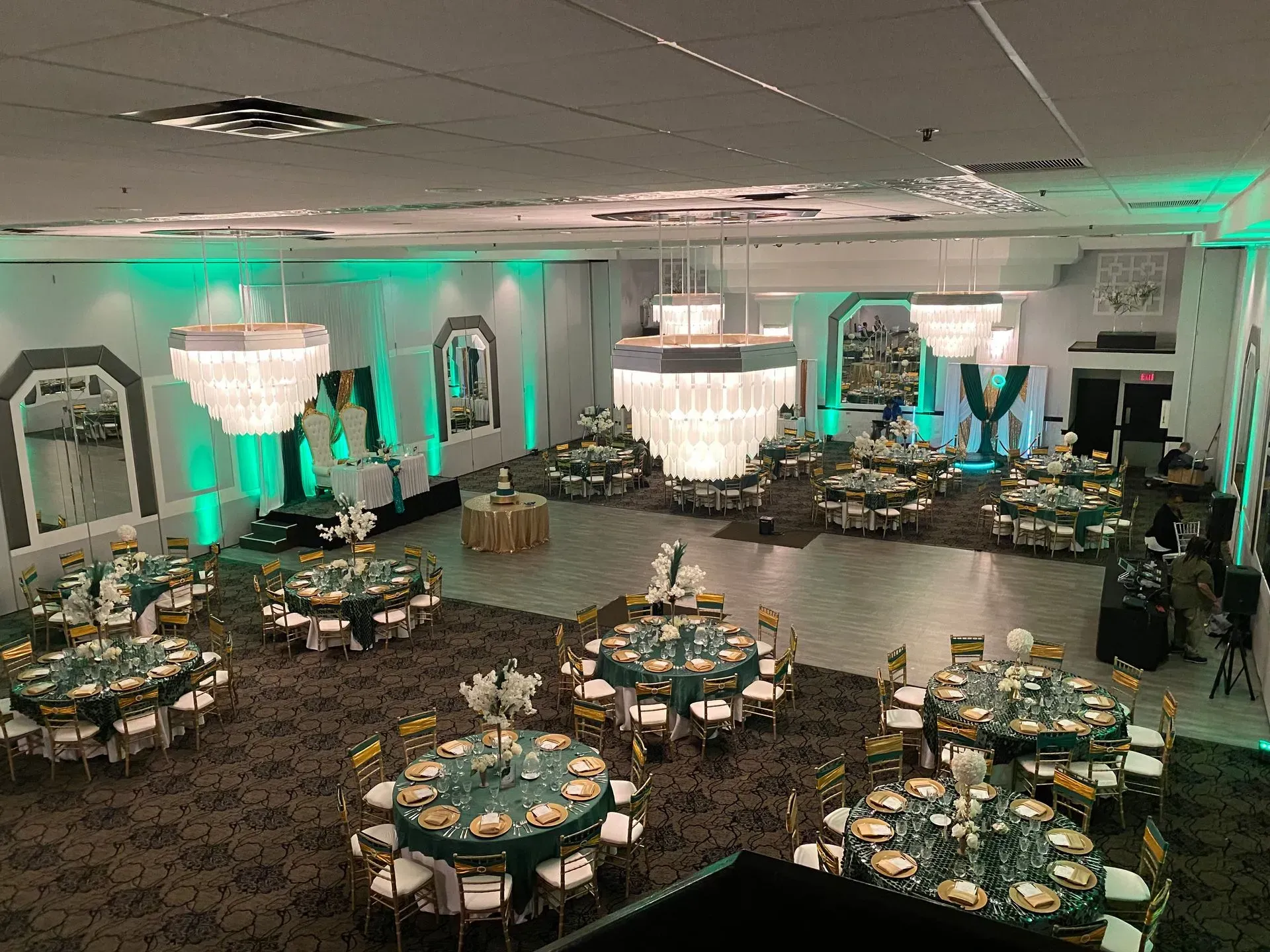 Elegant banquet hall with round tables set in teal and gold, lit by chandeliers and green accent lights
