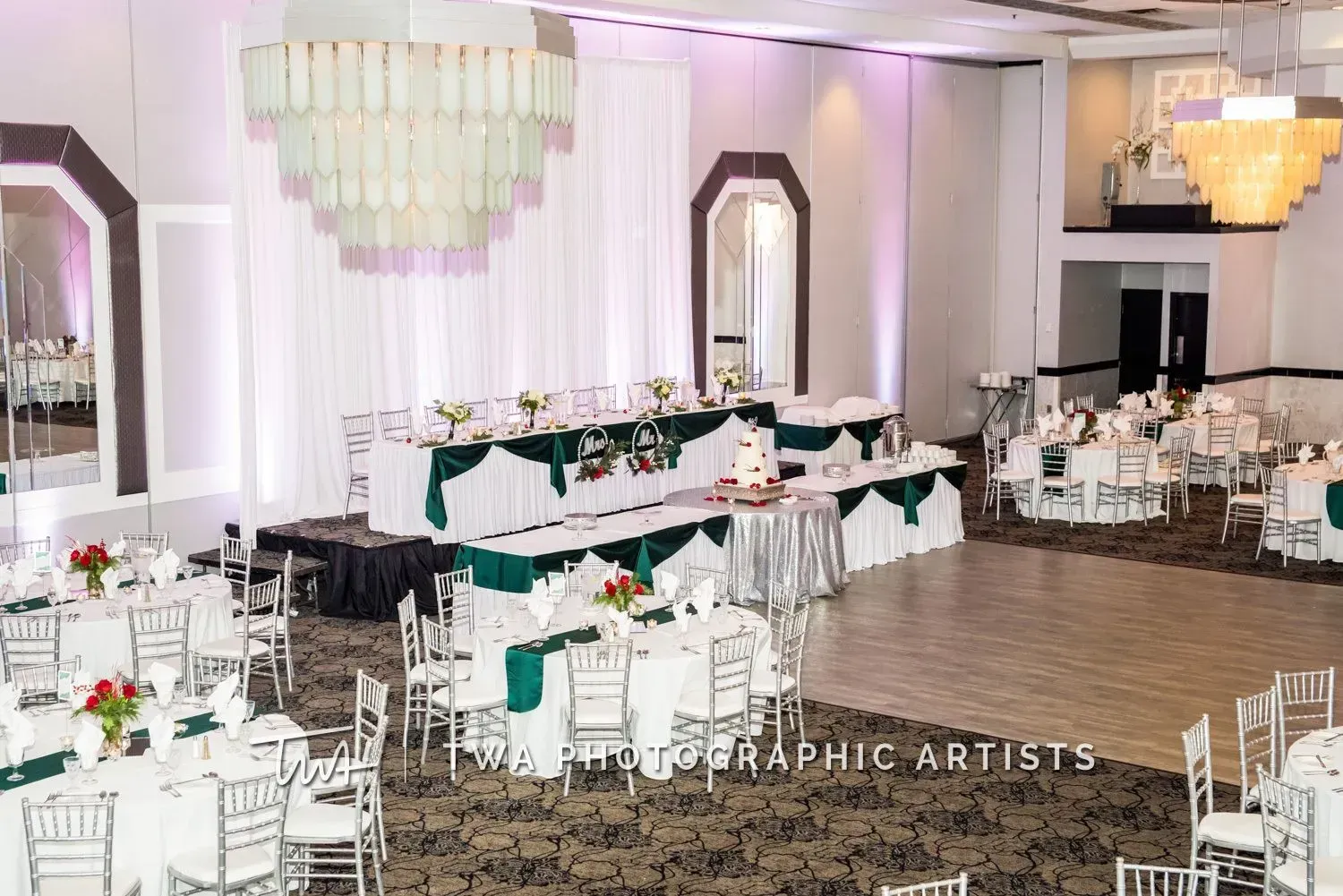 Elegant banquet hall with white tables, green accents, and chandeliers set for an event