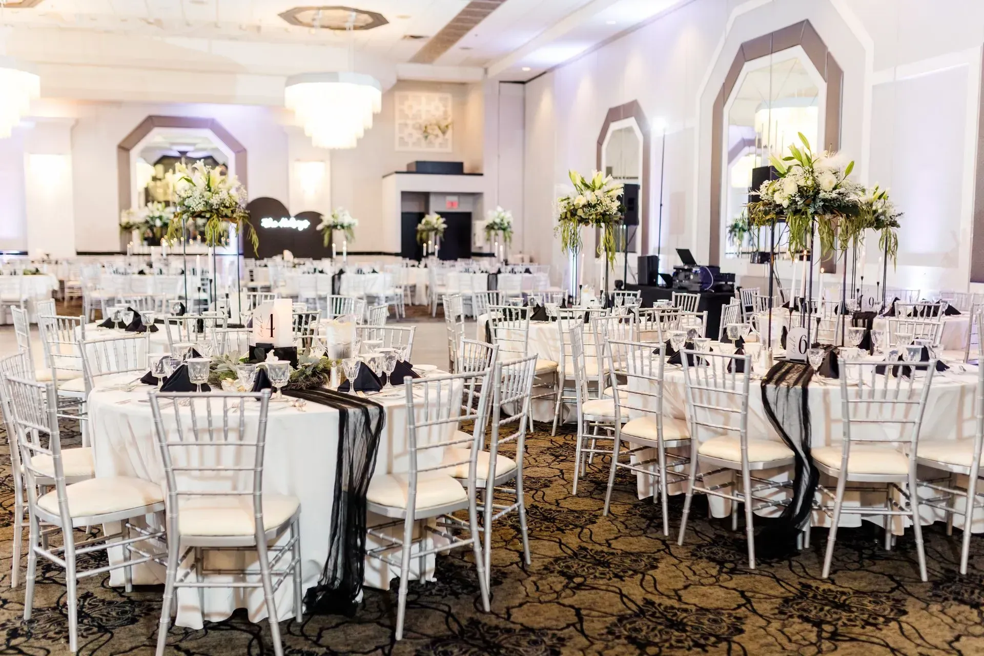 Banquet hall set for a formal event with round tables, white chairs, and tall floral centerpieces.