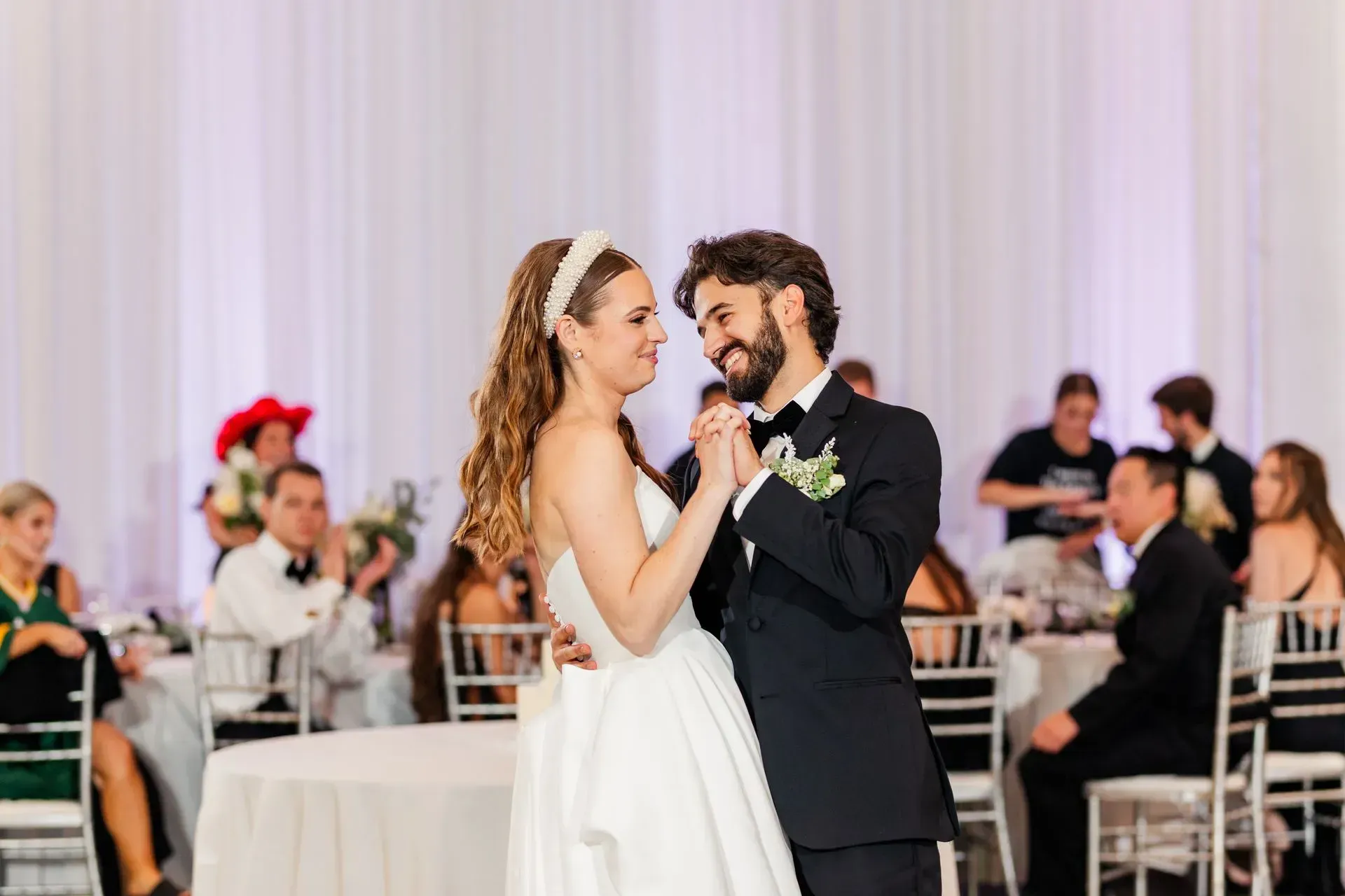 Bride and groom slow dancing at their wedding reception with guests seated in the background