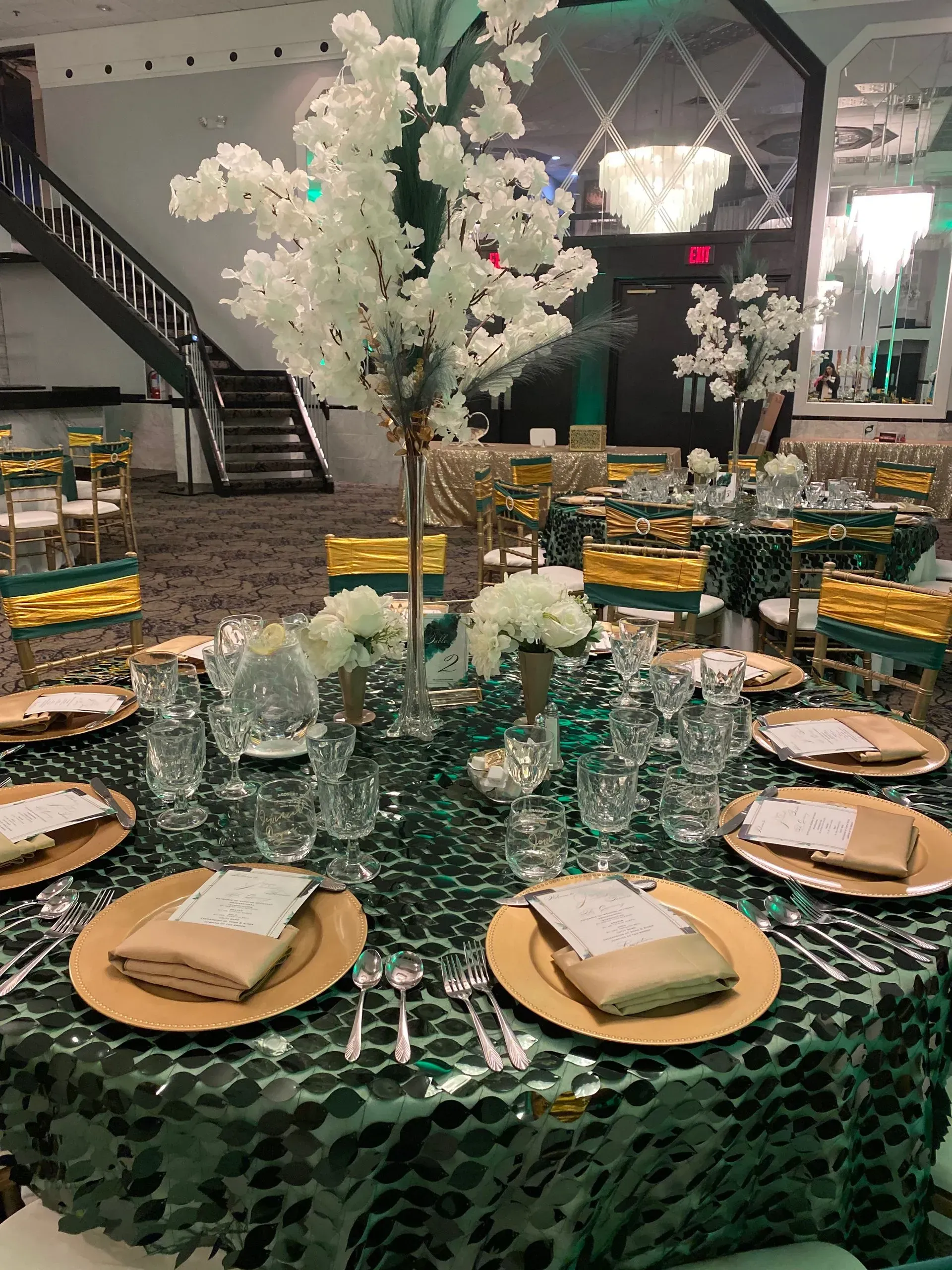 Elegant banquet table with green sequin cloth, gold plates, folded napkins, and white floral centerpiece