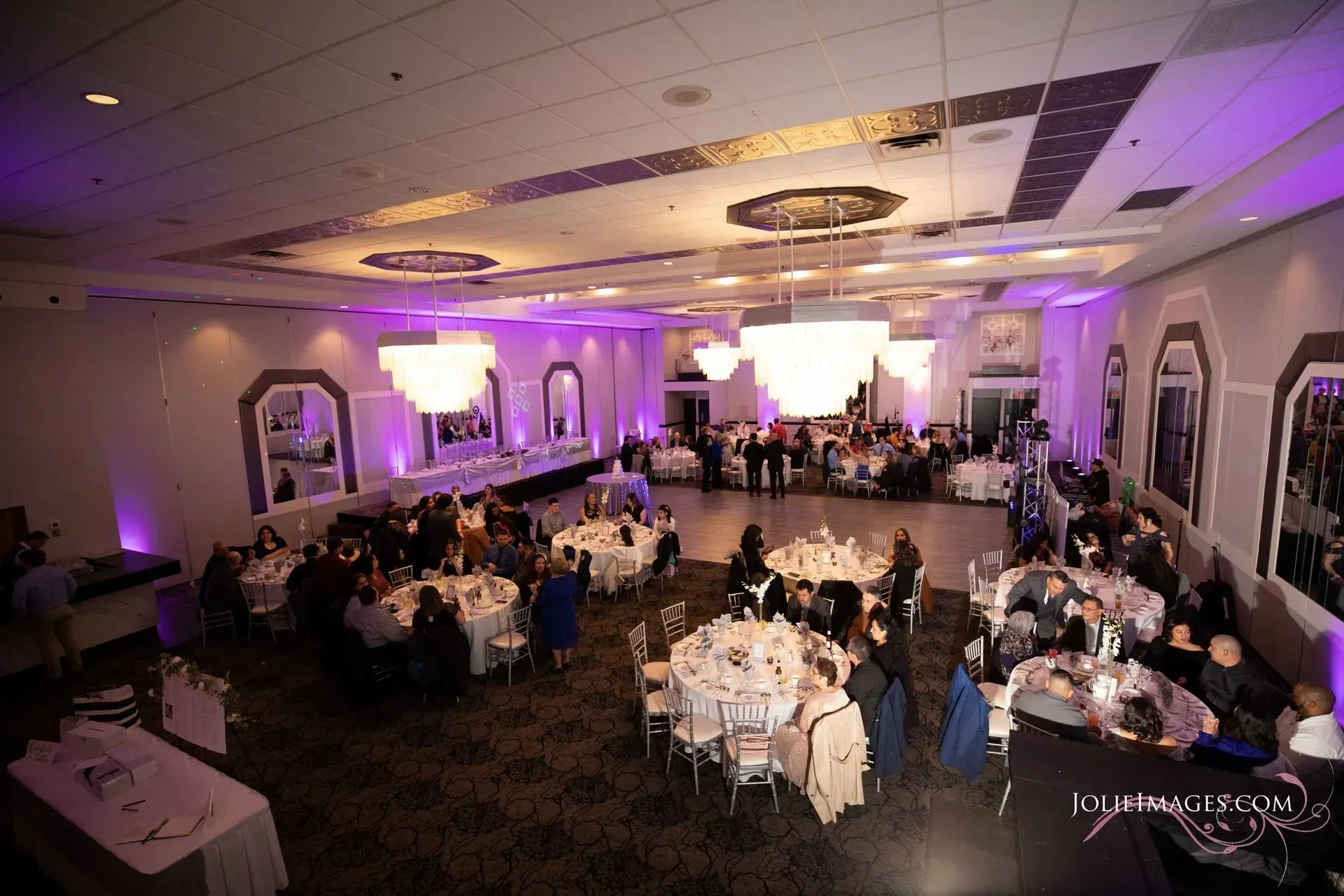 Banquet hall with round tables and guests dancing under purple lighting during a formal event