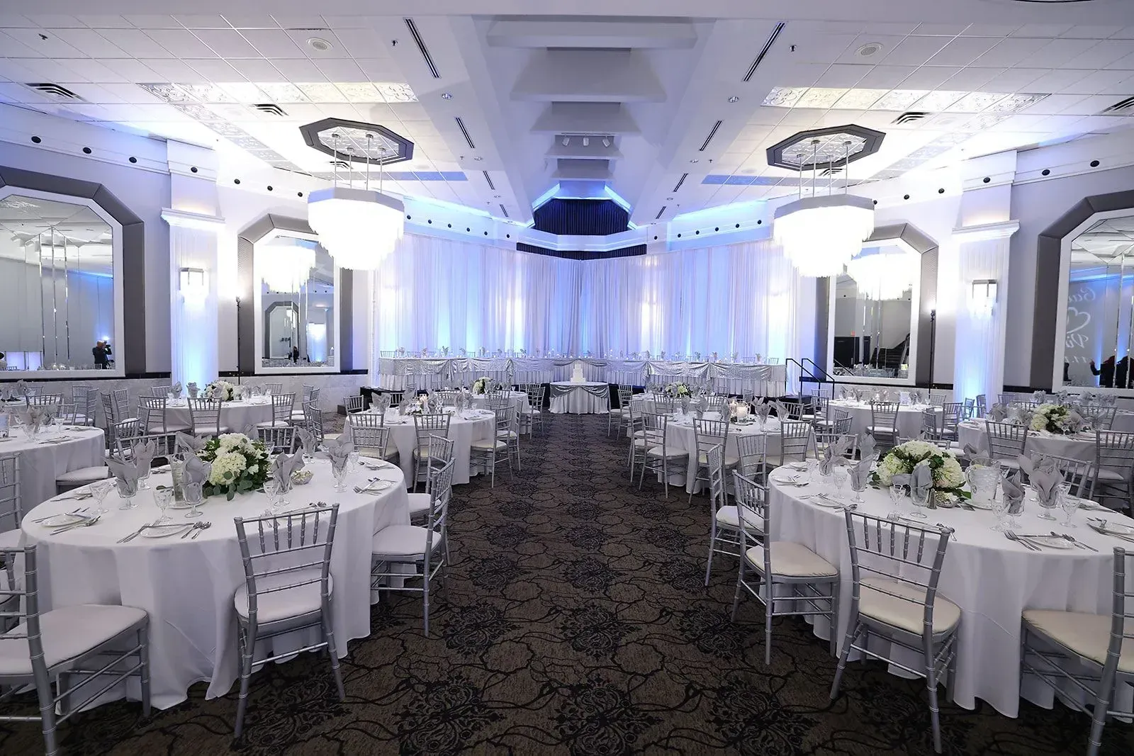 Elegant banquet hall with round tables, white chairs, and blue uplighting for a formal event