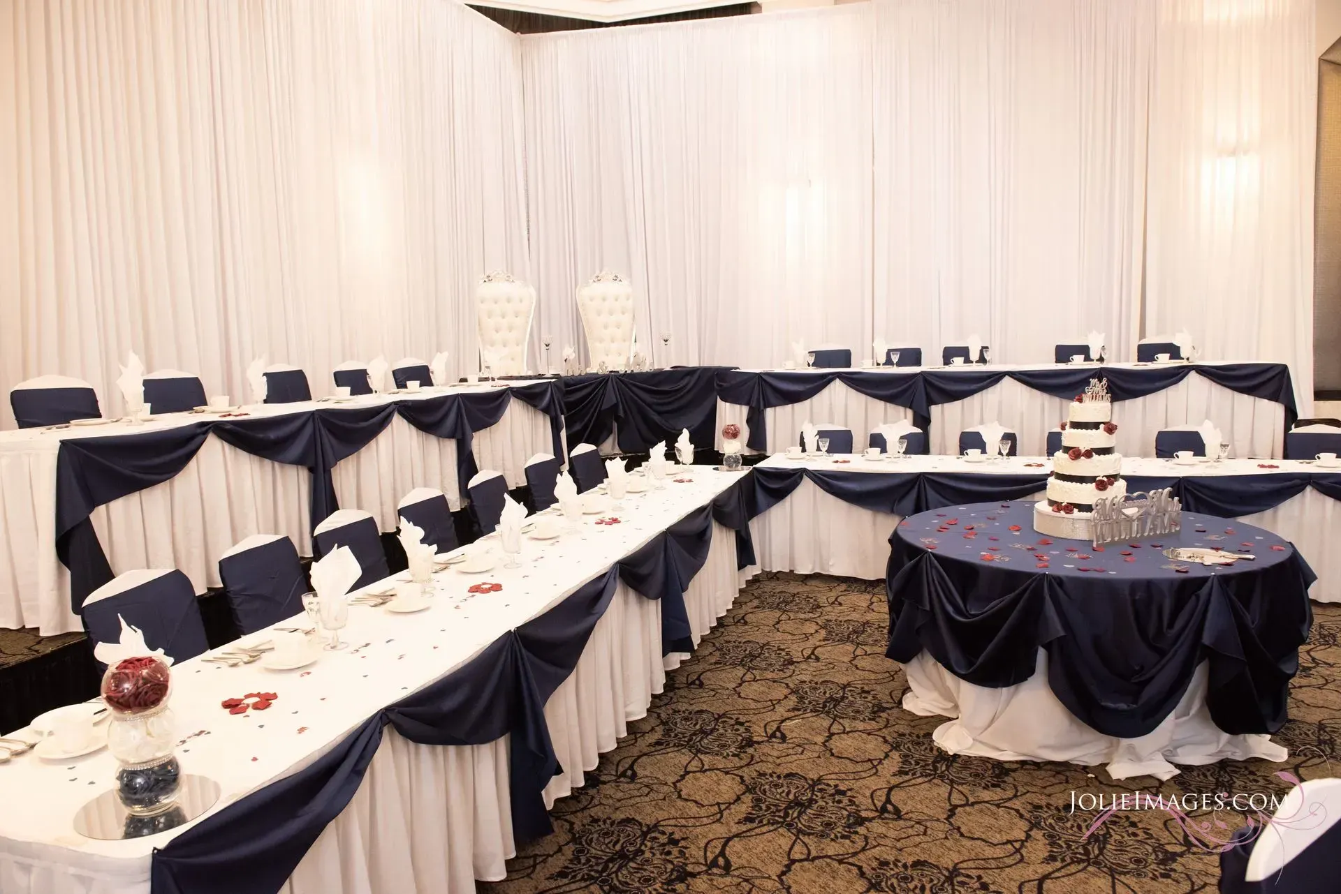 White-draped banquet room with U-shaped tables, chairs, and a round dessert display table