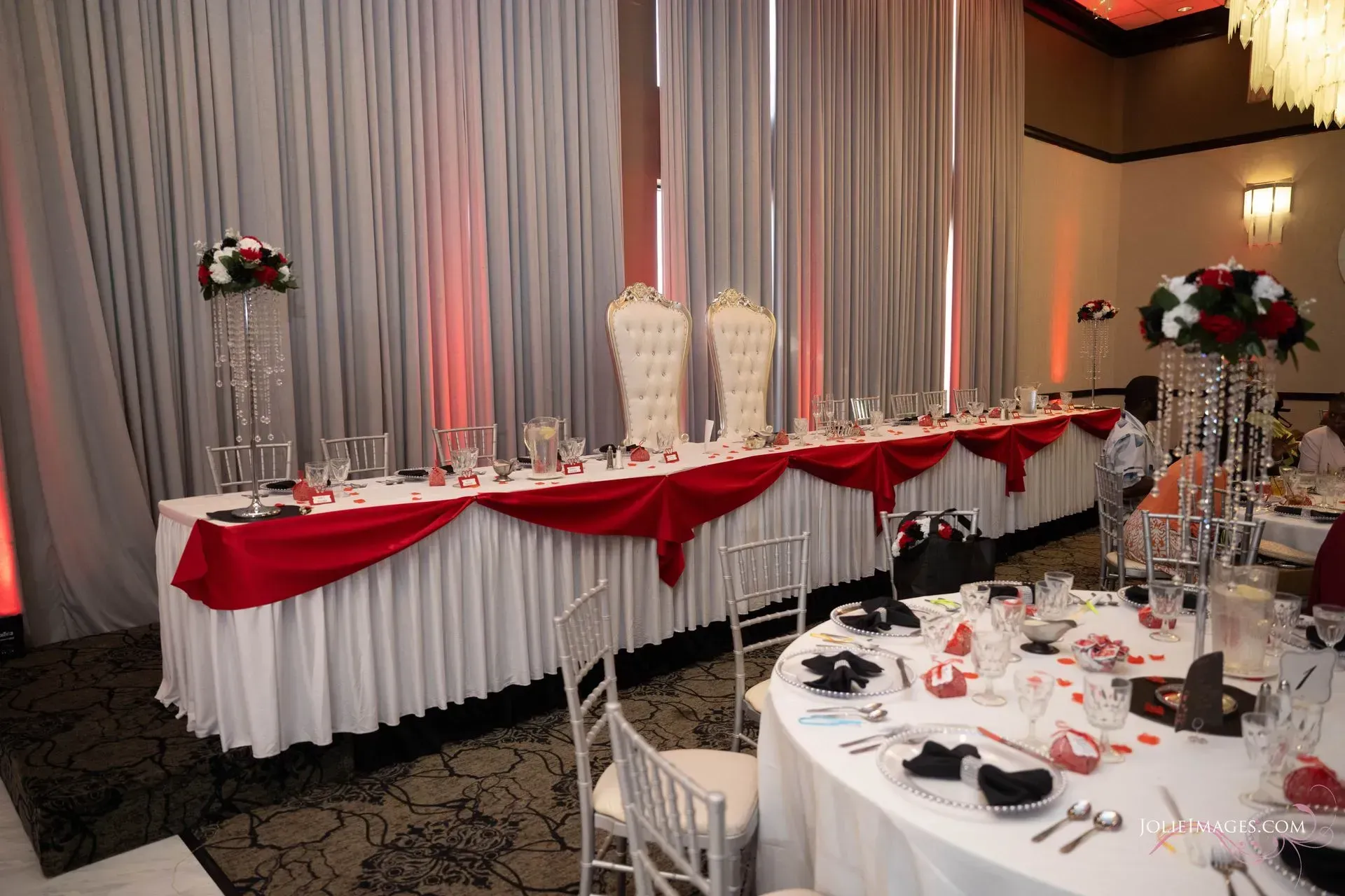 Elegant banquet hall setup with red-and-white draped tables and tall floral centerpieces