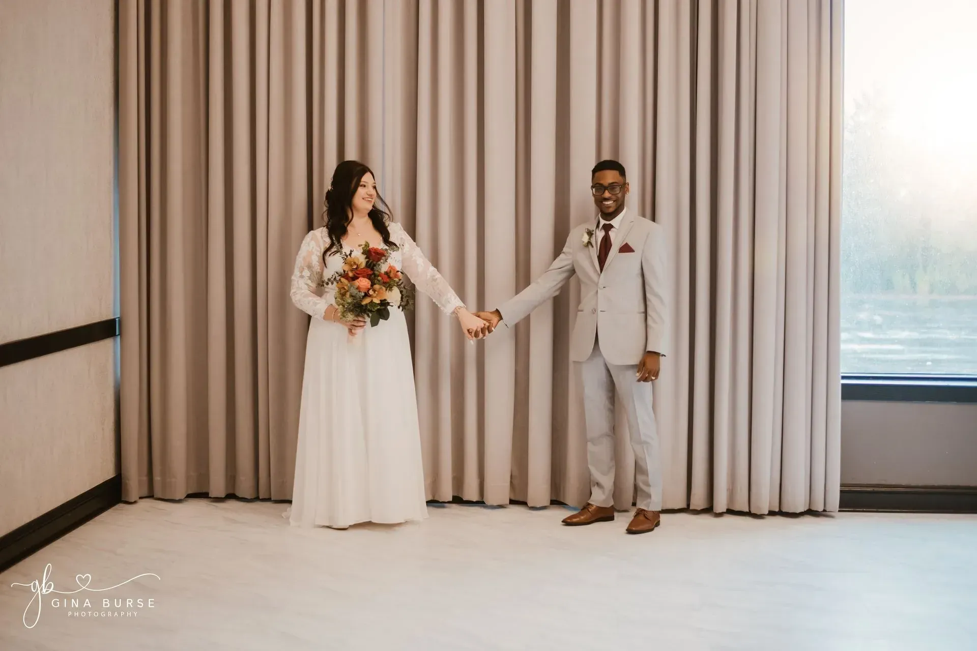 Bride and groom holding hands in front of beige curtains at an indoor wedding venue