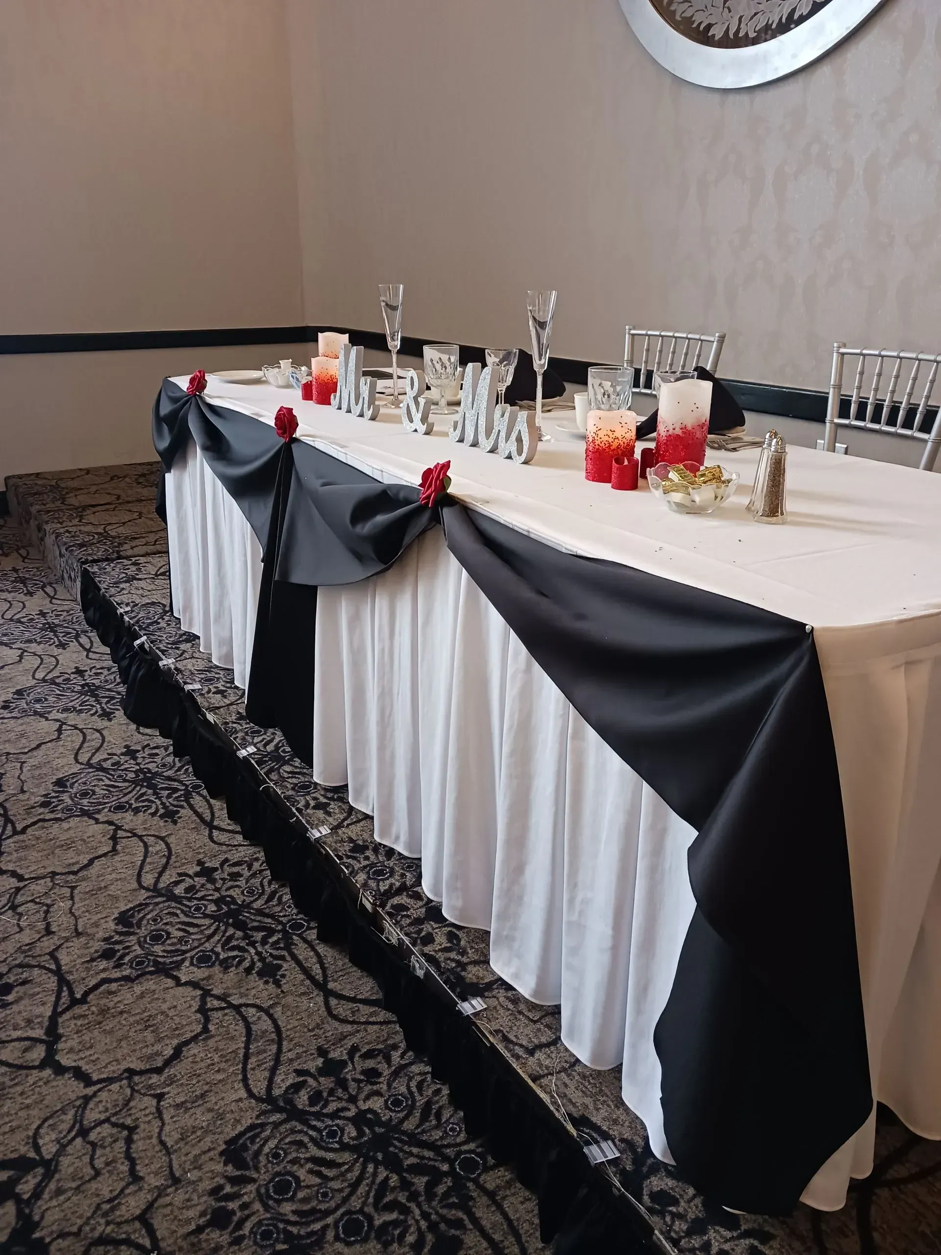 Decorated banquet table with black and white draping, candles, and glasses in a formal event room