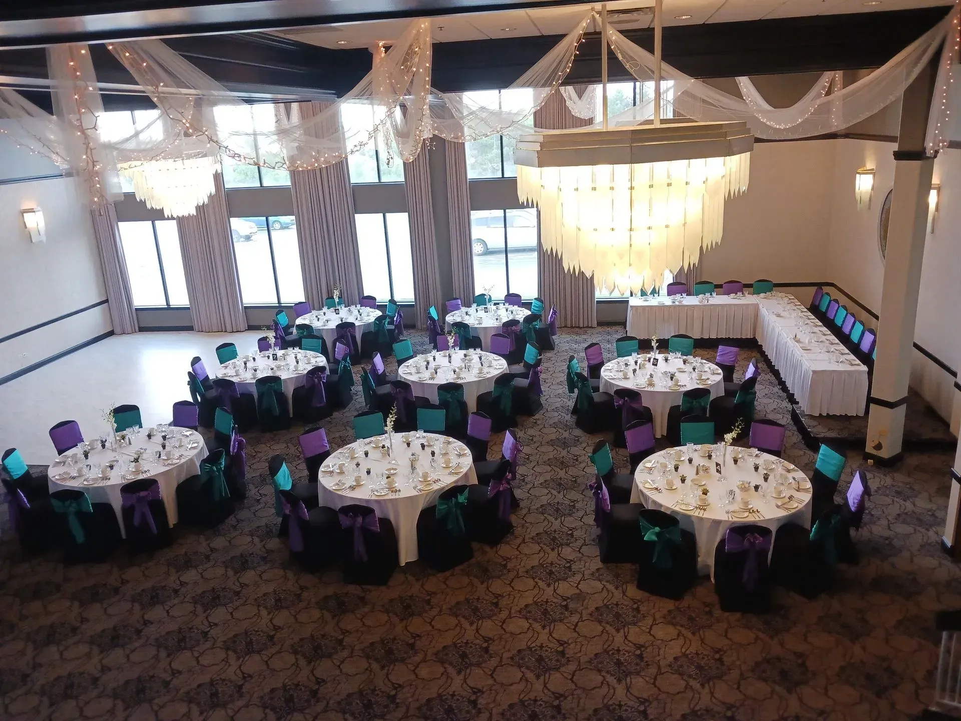 Banquet hall with round tables dressed in white and black chairs under warm hanging lights