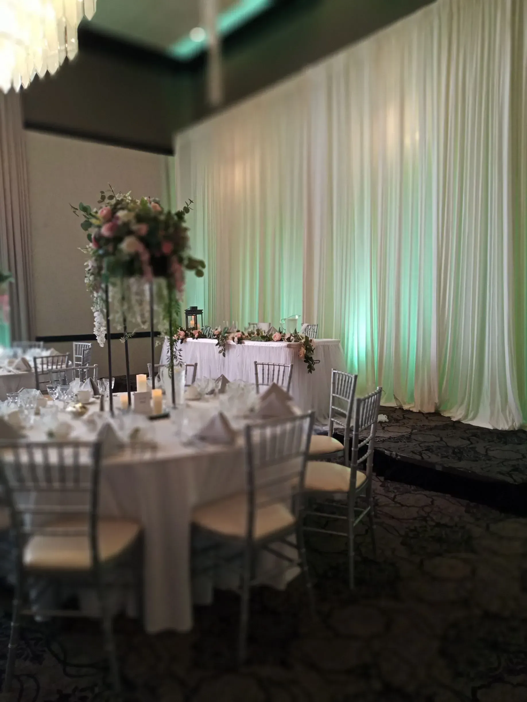 Round banquet tables with white linens and floral centerpieces in a softly lit event hall with green drapes