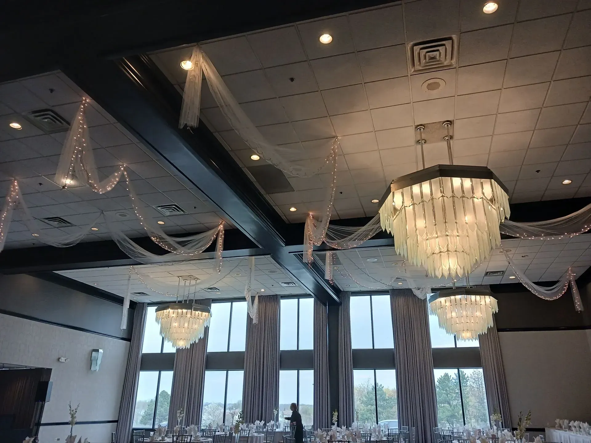Elegant banquet hall ceiling with chandeliers, draped fabric, and tall windows