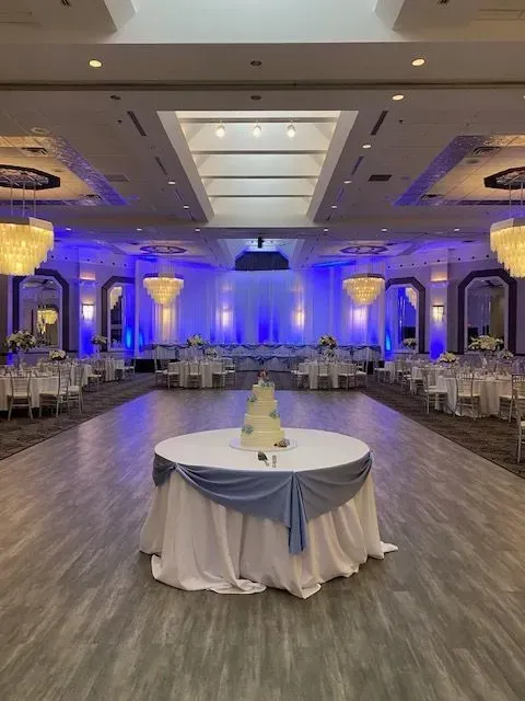 Elegant banquet hall with blue uplighting, round tables, and a decorated centerpiece in the foreground