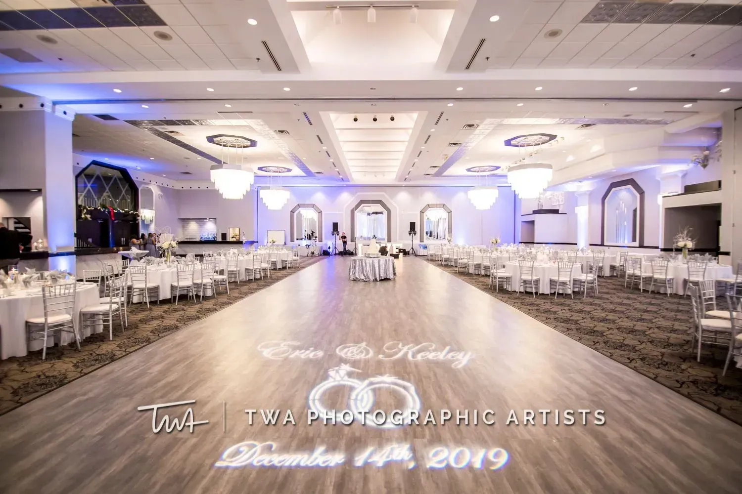 Elegant empty wedding reception hall with white tables, chairs, chandeliers, and a dance floor