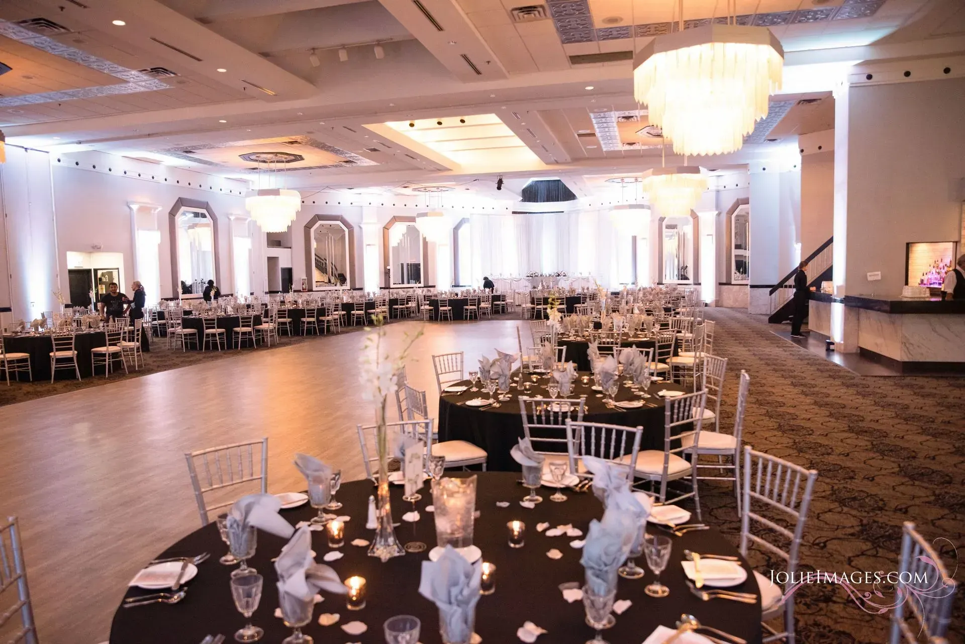 Elegant banquet hall with round tables, white chairs, chandeliers, and a polished wooden dance floor