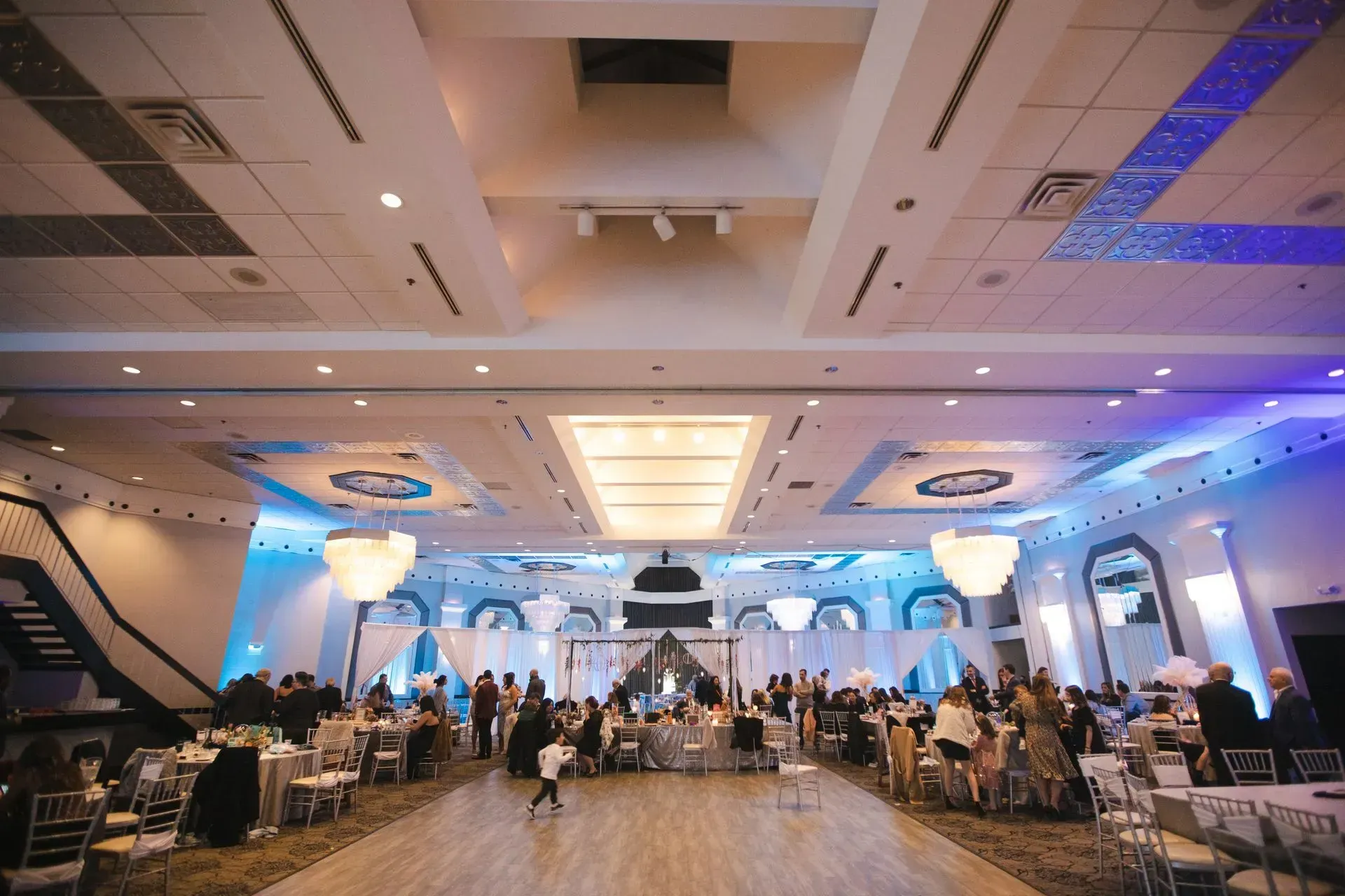 Large banquet hall with round tables, seated guests, and blue accent lighting under a high ceiling