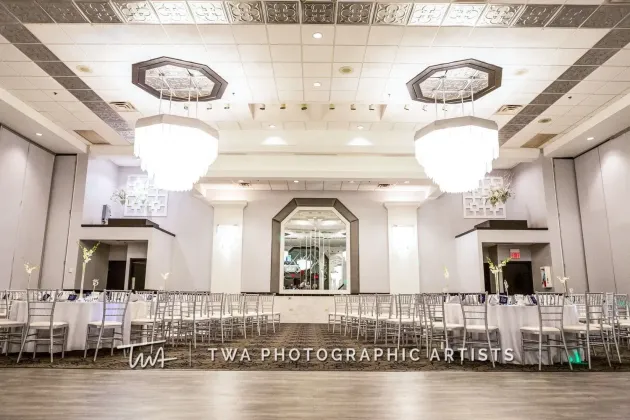 Elegant banquet hall with chandeliers, mirrored wall, and rows of white chairs set up for an event