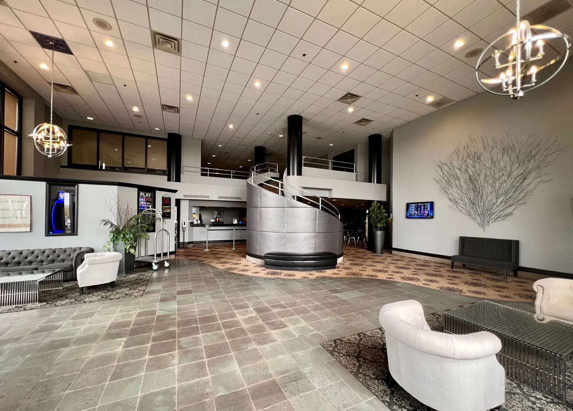 Spacious hotel lobby with curved reception desk, lounge chairs, tiled floor, and chandelier lighting