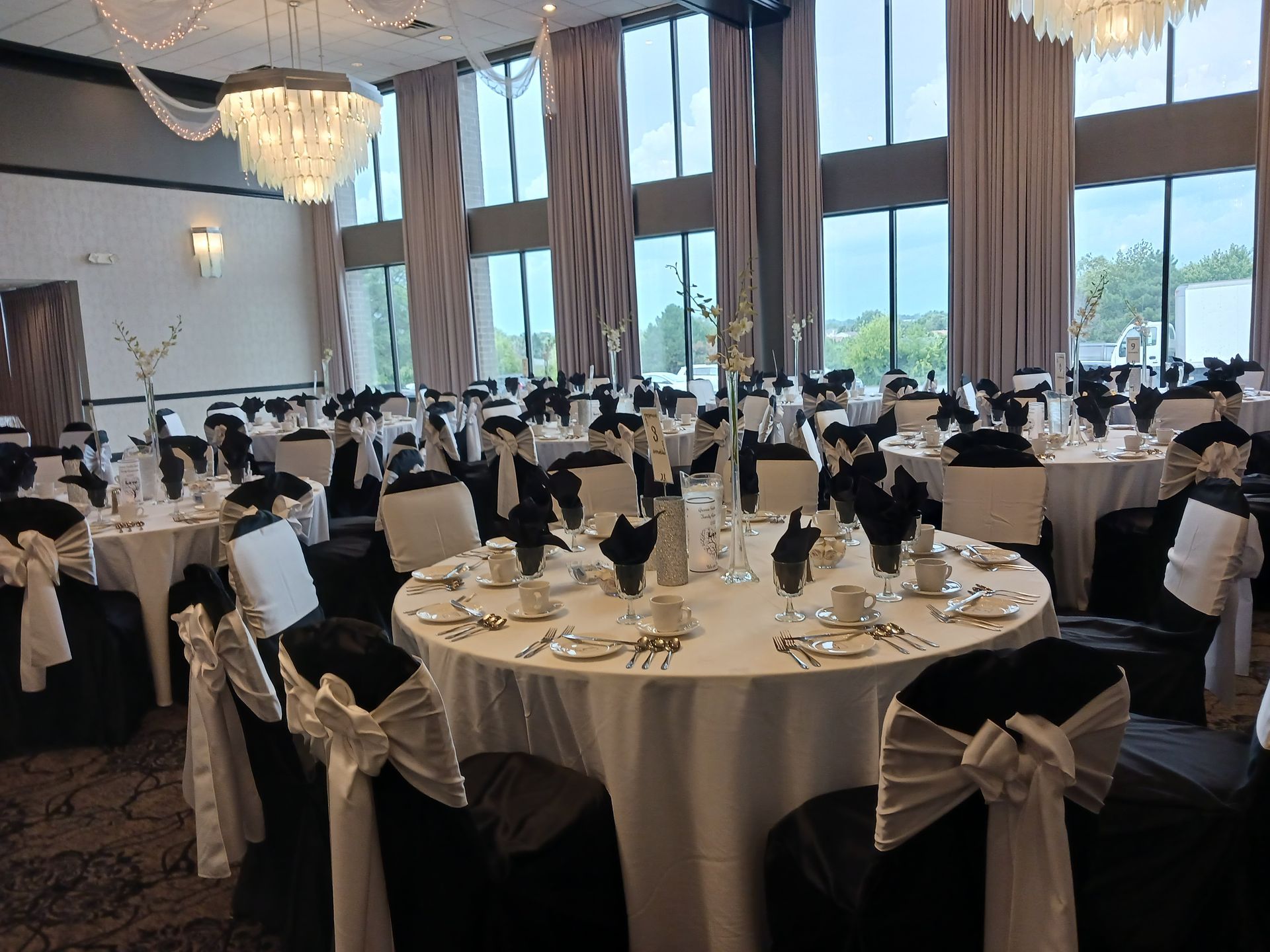 Elegant banquet hall with round tables, white chairs, and large windows overlooking a scenic outdoor view