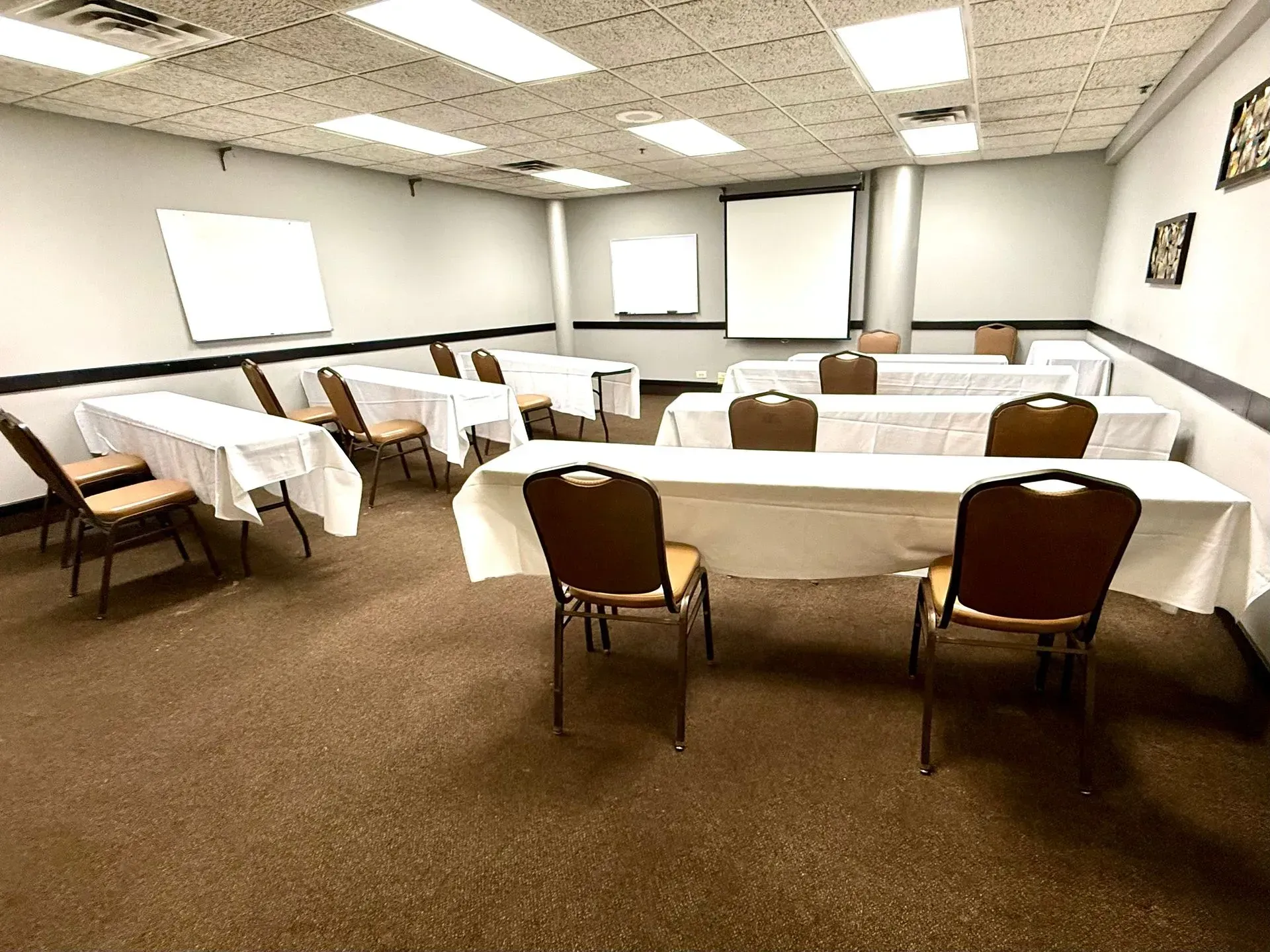 Empty conference room with tables draped in white cloths and brown chairs under fluorescent lights.