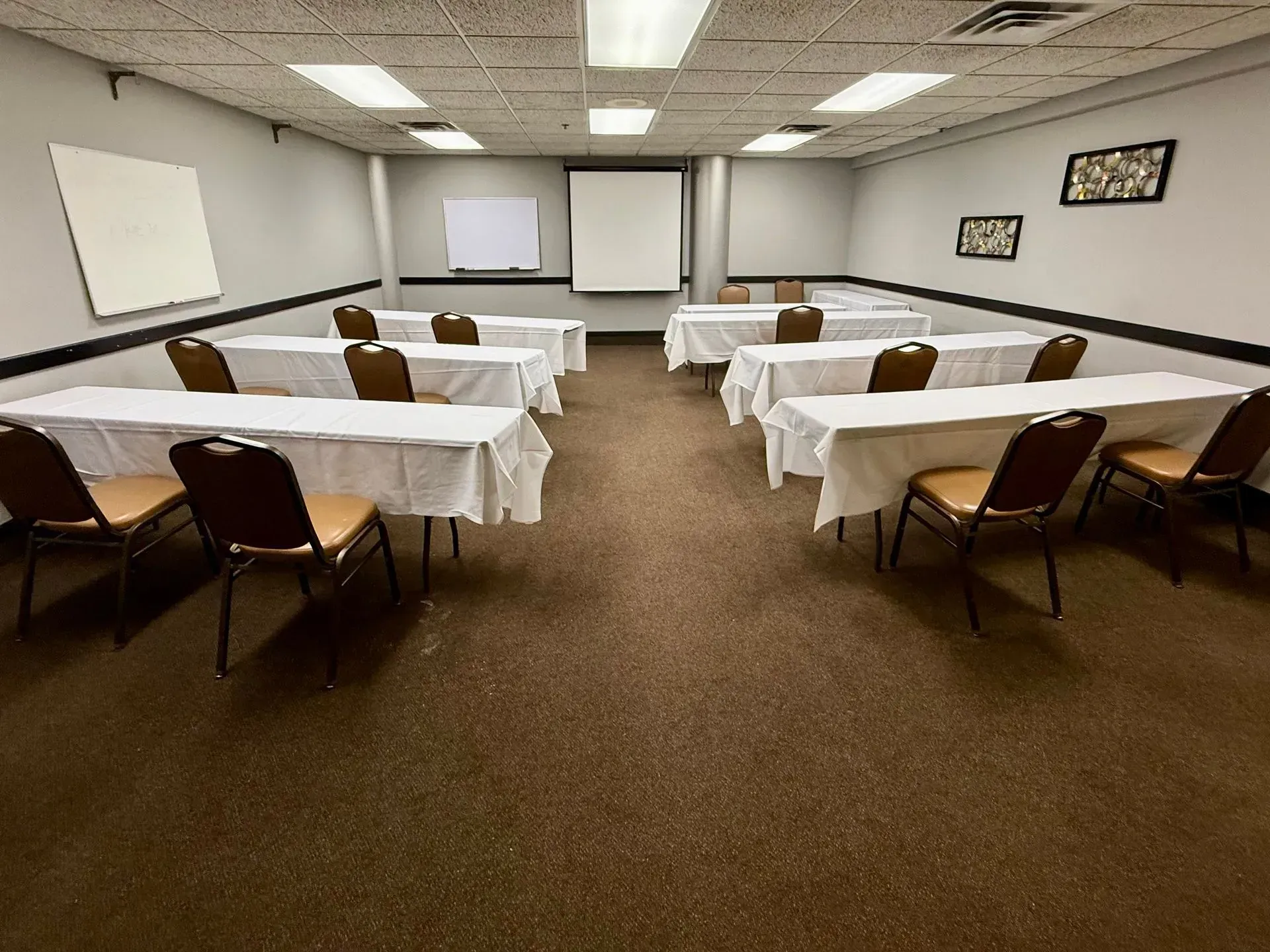 Empty conference room with rows of tables, brown chairs, projector screens, and a whiteboard